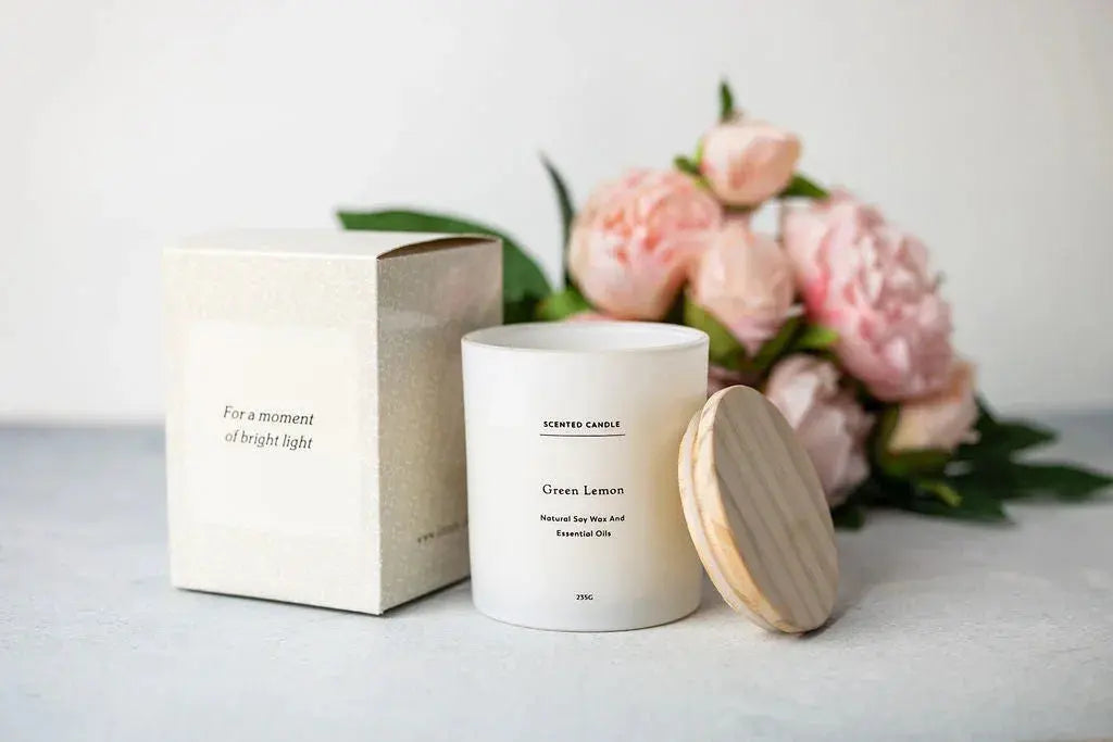 Green Lemon scented candle in white jar with wooden lid, beside gift box and pink peonies, cozy farmhouse decor