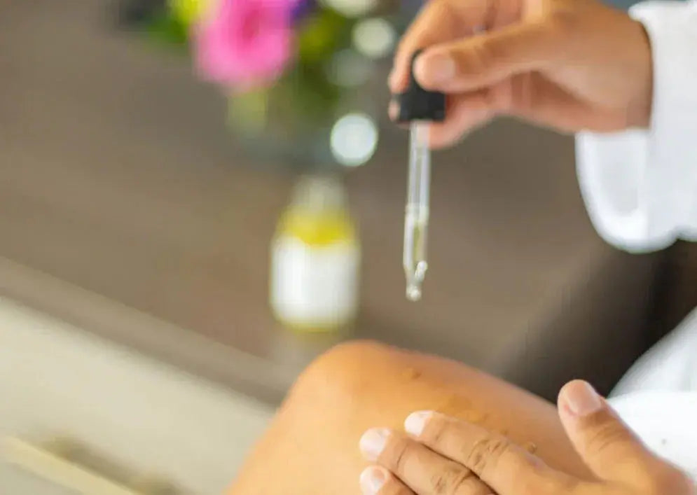 Dropper applying bath oil to skin, cozy self-care moment with floral background