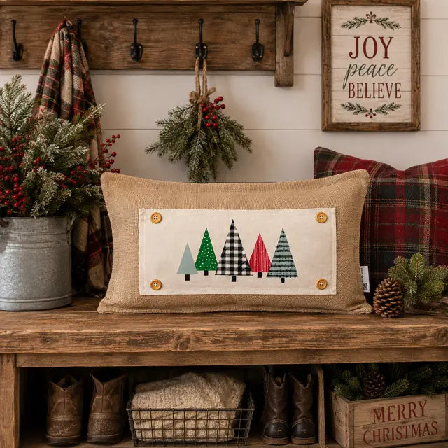 A rustic burlap throw pillow with a patchwork tree design, styled on a wooden bench in a cozy holiday room setting.