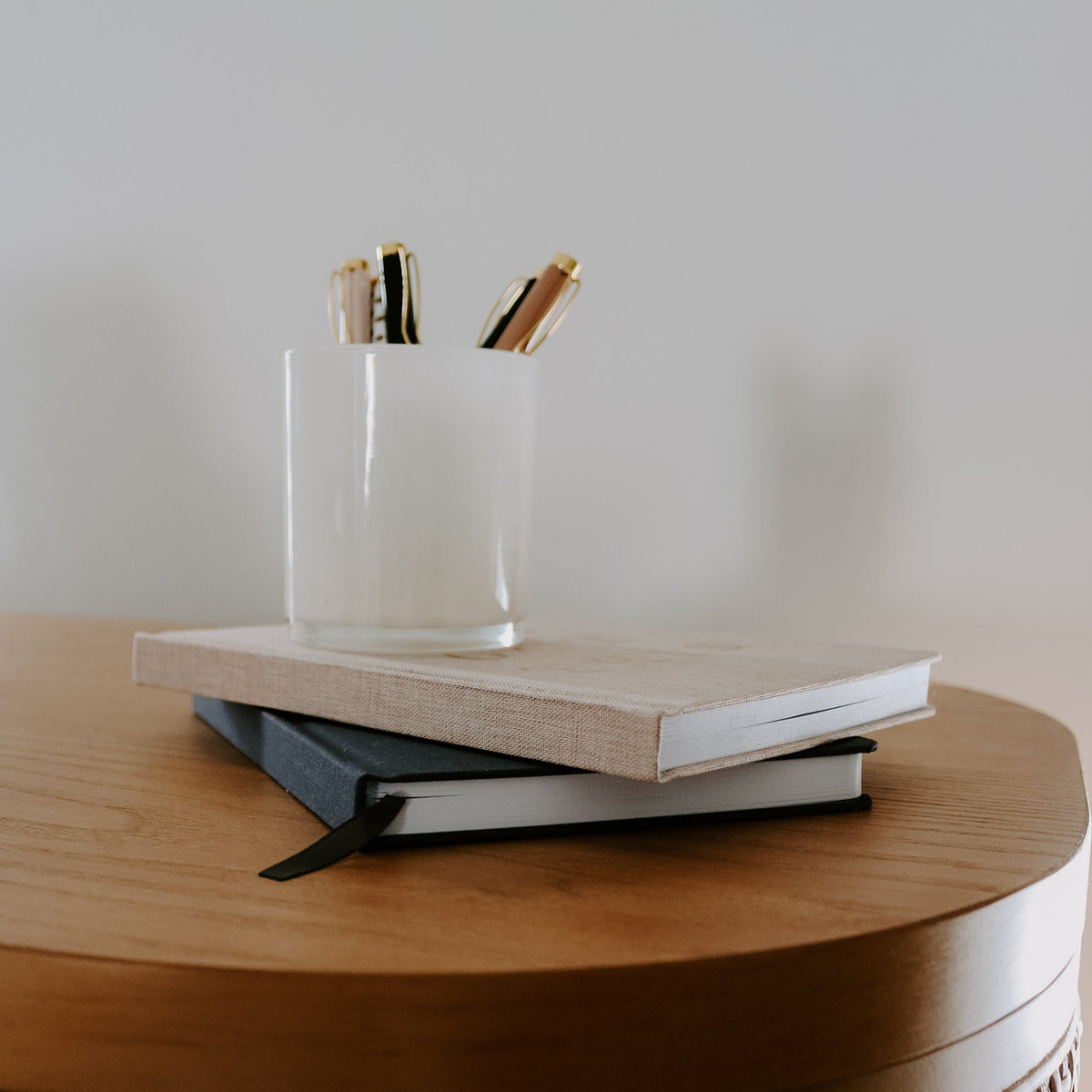 Stack of books with a glass and pens on a wooden surface