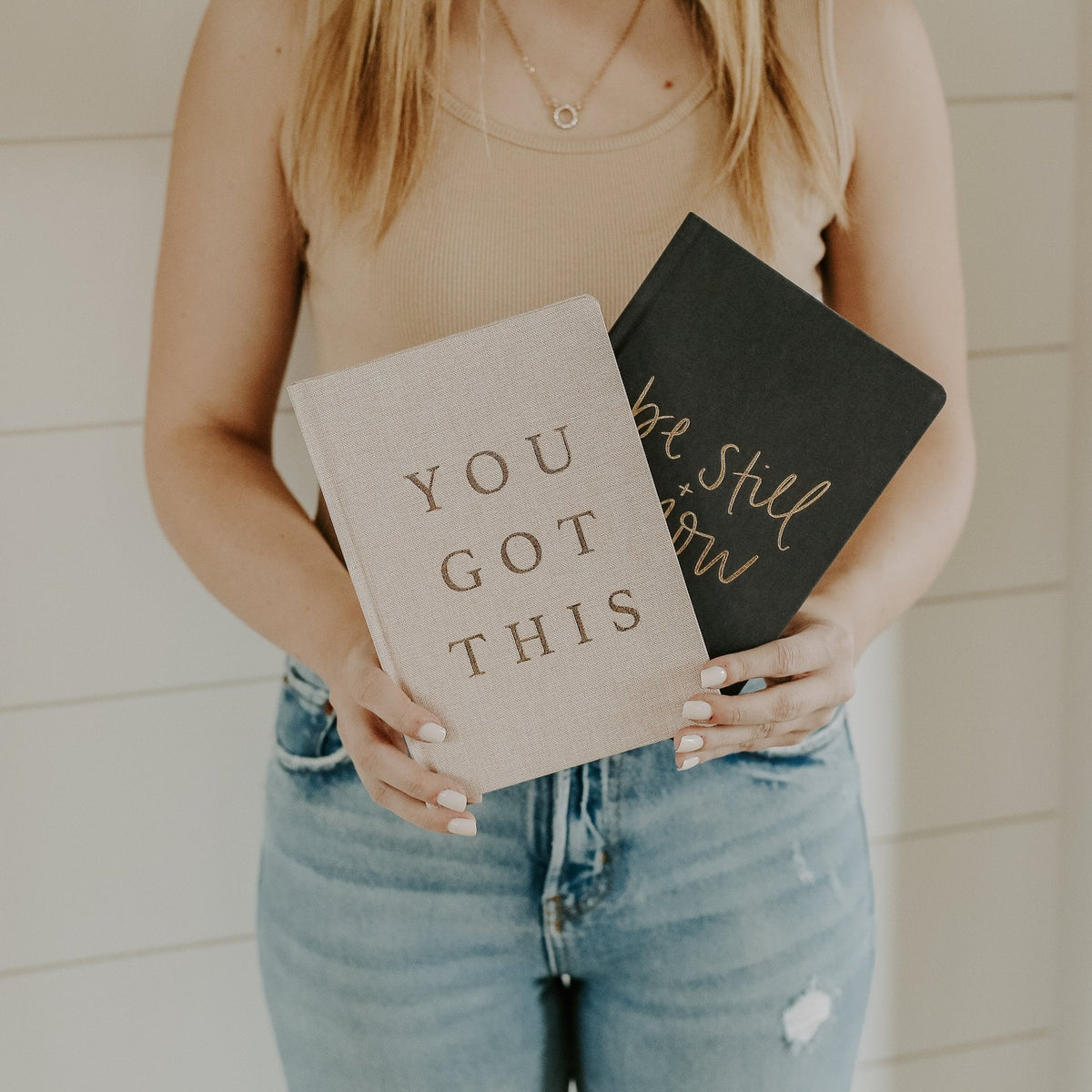 Person holding two books with motivational phrases against a neutral background