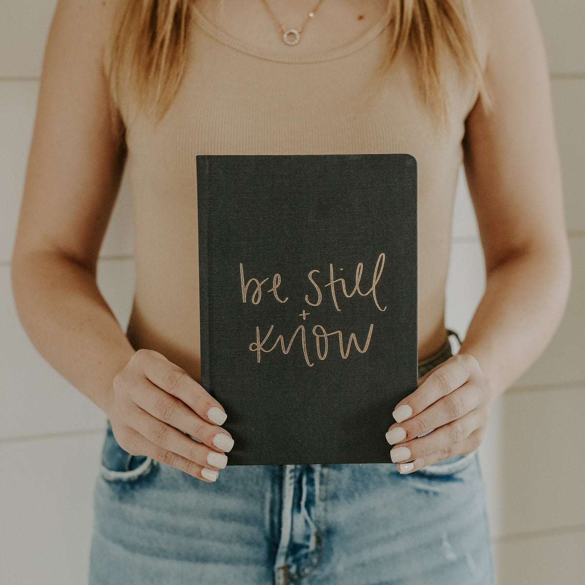 Person holding a black notebook with 'be still and know' text.