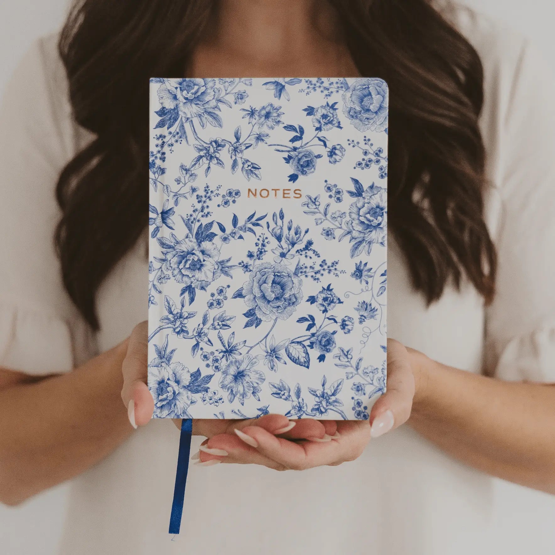 Person holding a blue floral notebook with 'NOTES' text
