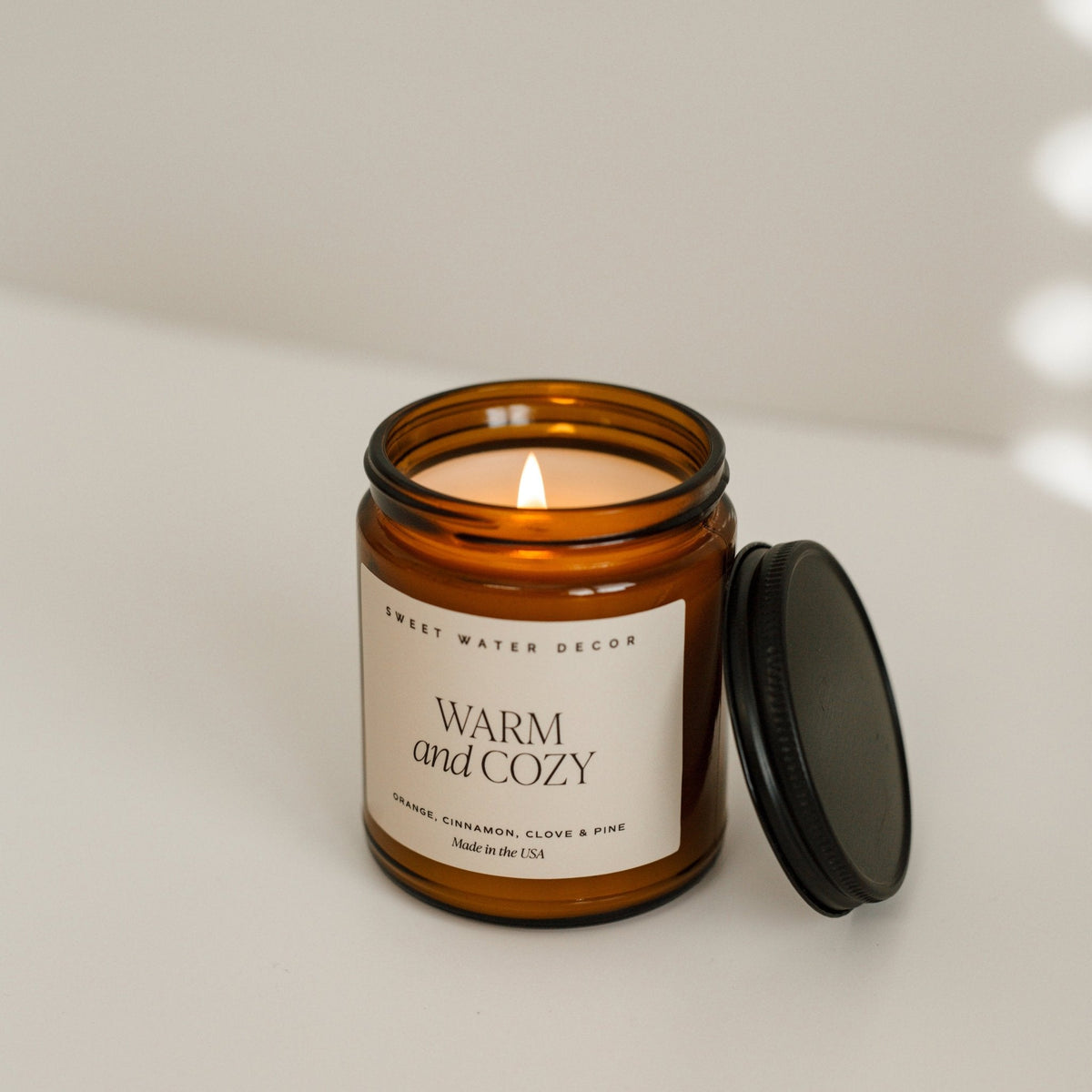 Candle in an amber jar with a label on a neutral background Warm and Cozy