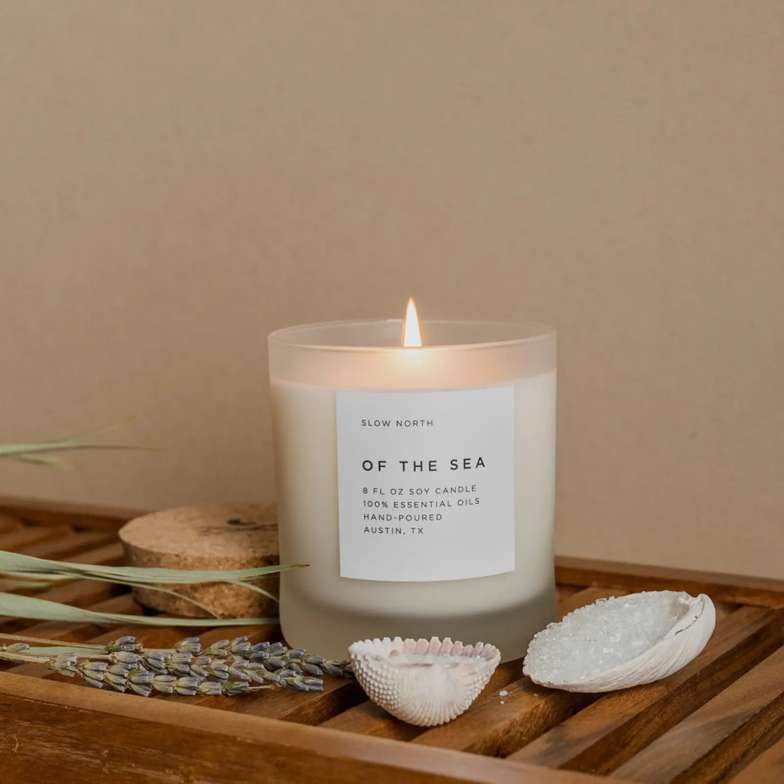 Candle labeled 'Of the Sea' by Slow North on a wooden surface with decorative elements.