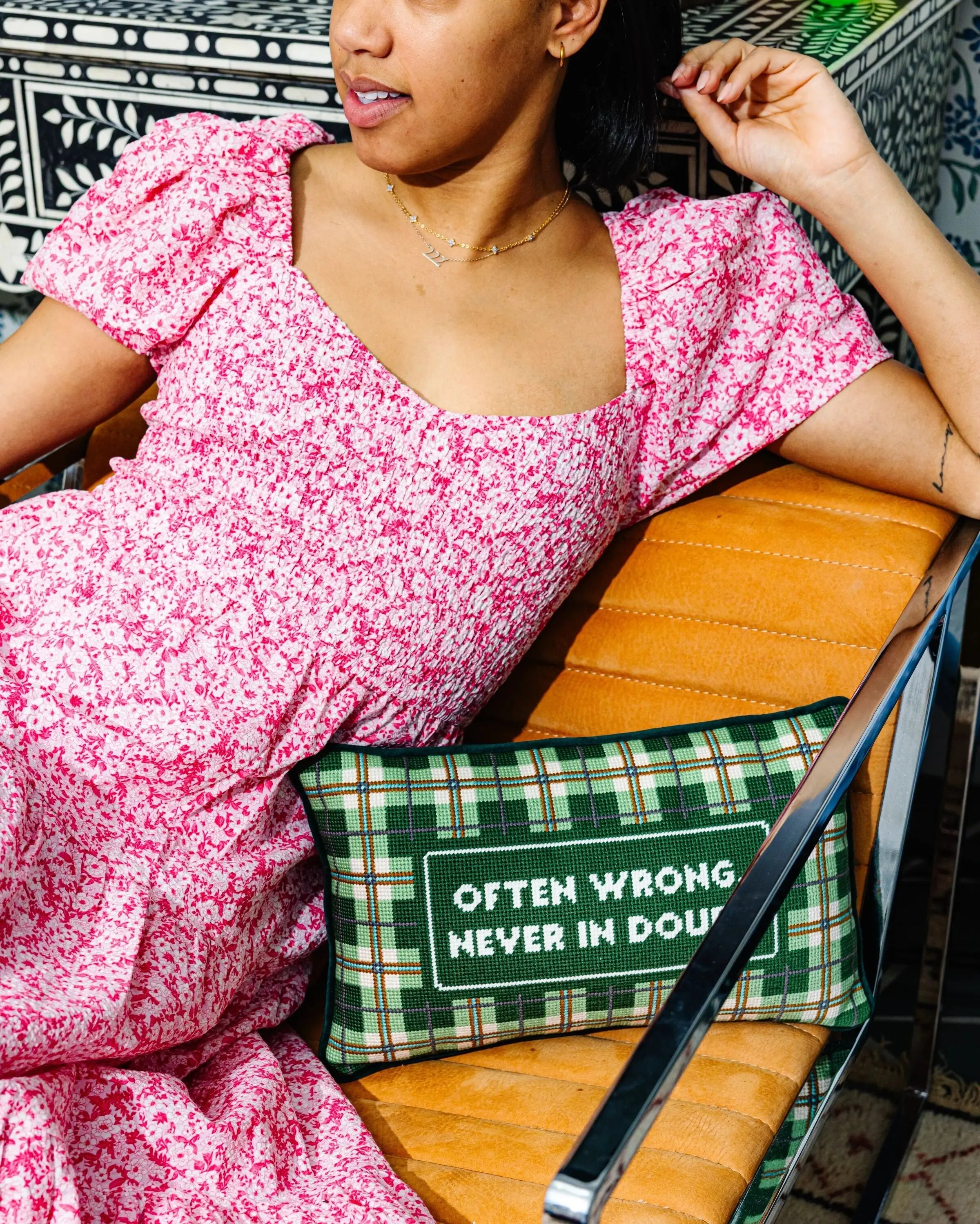 Woman in a pink floral dress sitting on a chair with a green plaid pillow.