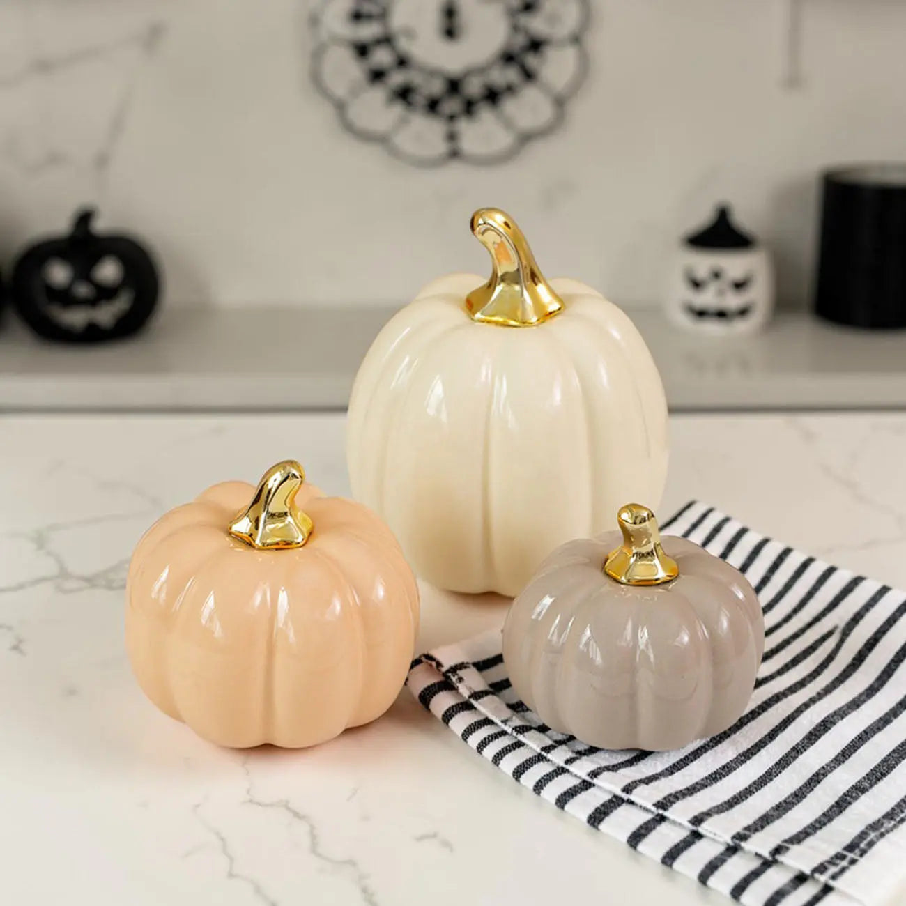 Three decorative pumpkins with gold stems on a marble surface with a striped towel.
