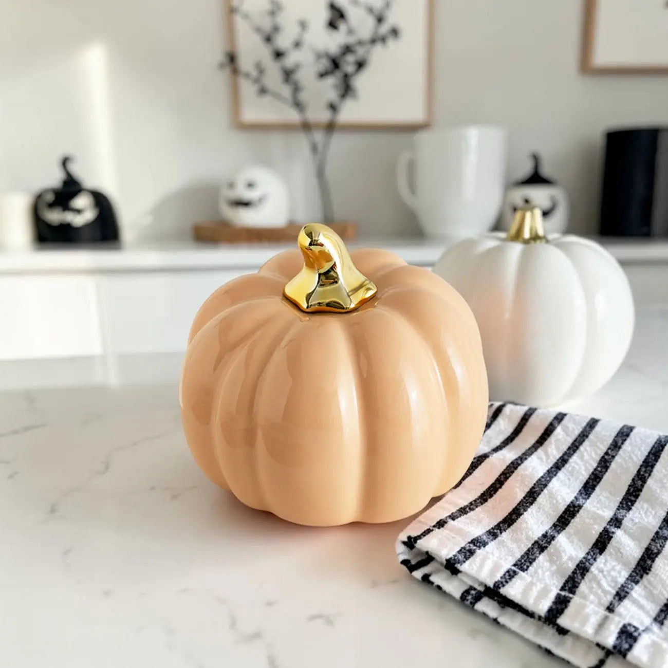 Decorative pumpkin with a gold top on a marble surface, with a white and black striped towel nearby.
