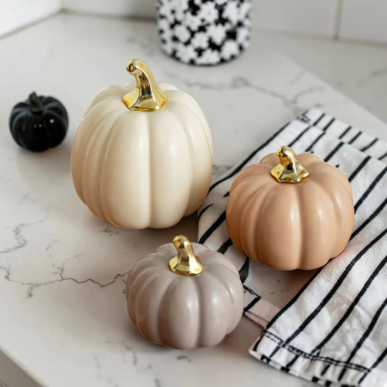 Decorative pumpkins in beige, brown, and gold on a marble surface with a striped cloth.