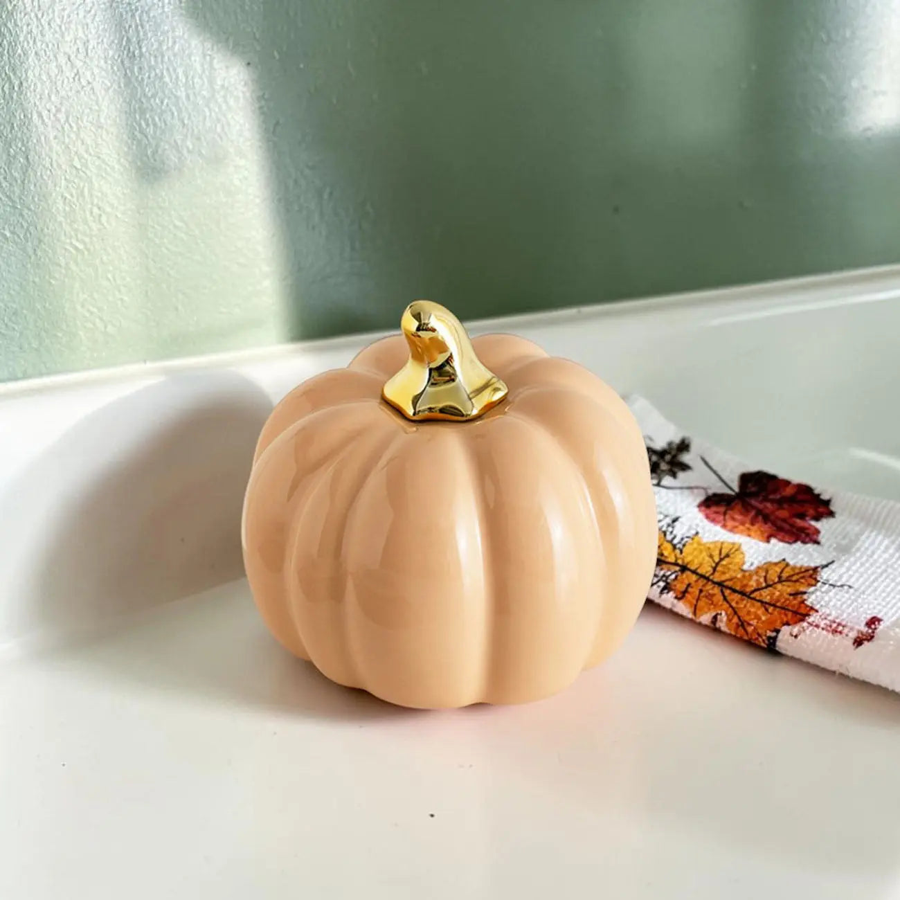 Decorative pumpkin with a gold top on a white surface with a green wall background