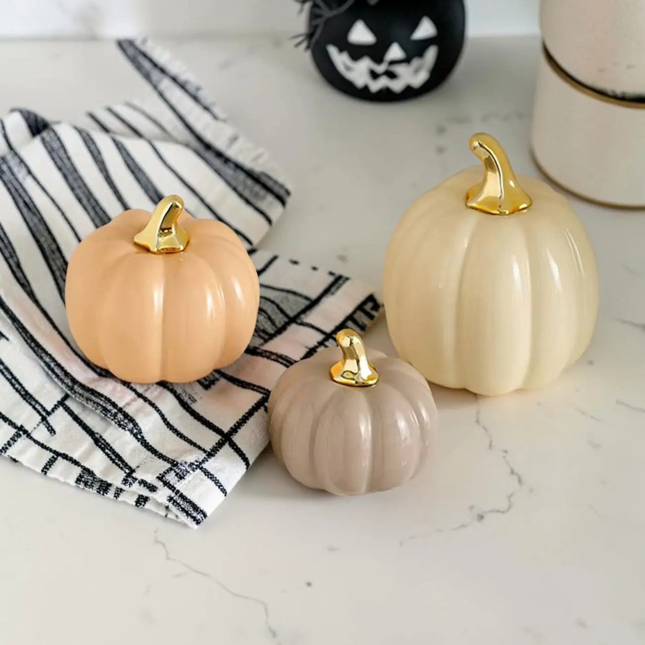 Three decorative pumpkins with gold stems on a marble surface with a striped cloth.