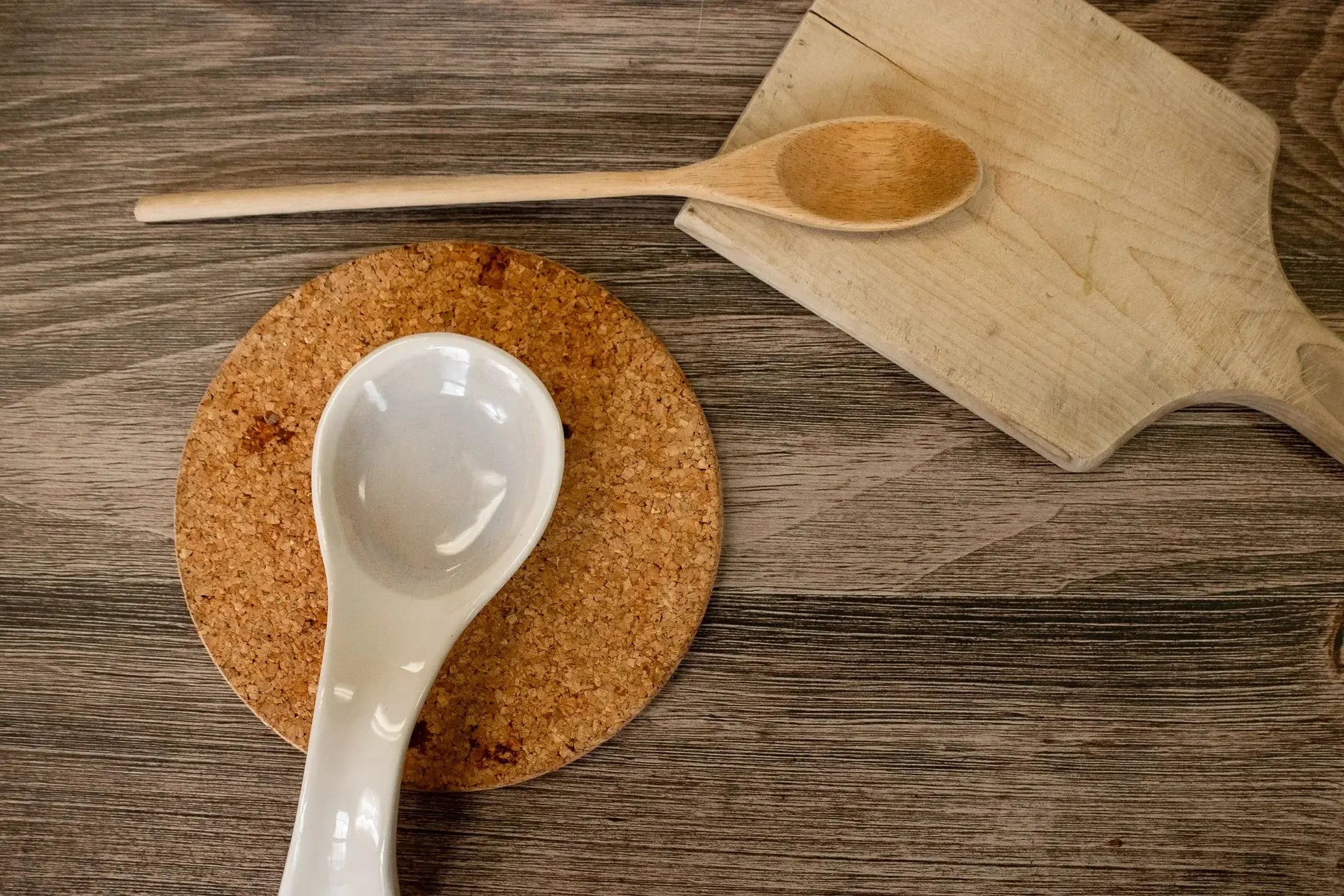 White ceramic and wooden spoons on cork coaster and cutting board, rustic kitchen decor
