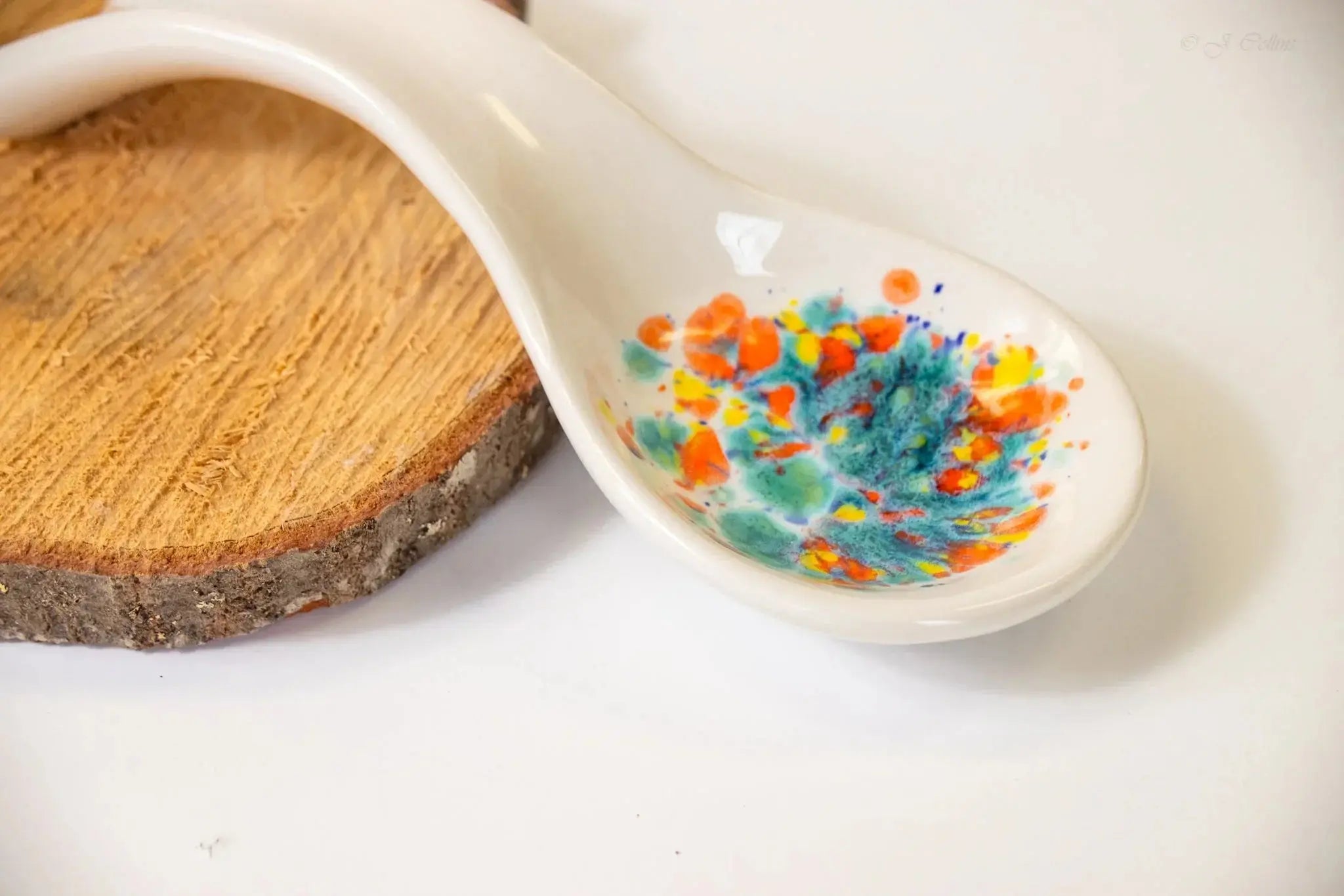 Hand-painted ceramic spoon with colorful floral design, rustic wood slice, cozy farmhouse decor