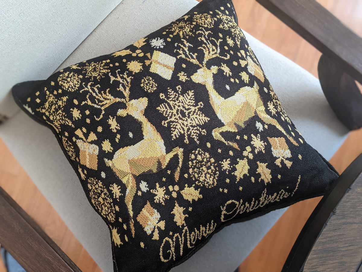 Decorative pillow with gold reindeer and floral patterns on a black background, featuring 'Merry Christmas' text.