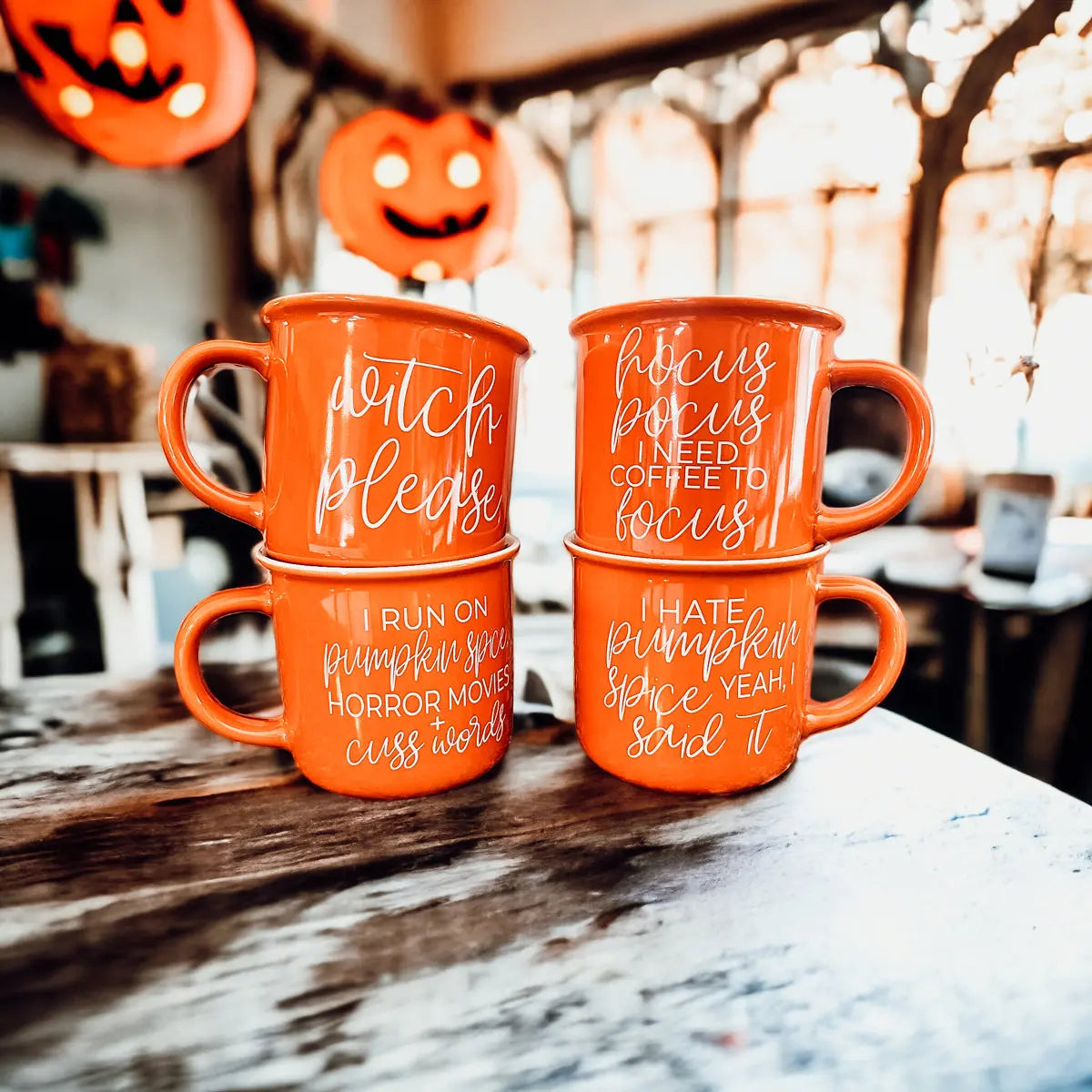 Stack of orange mugs with Halloween-themed text on a wooden table.