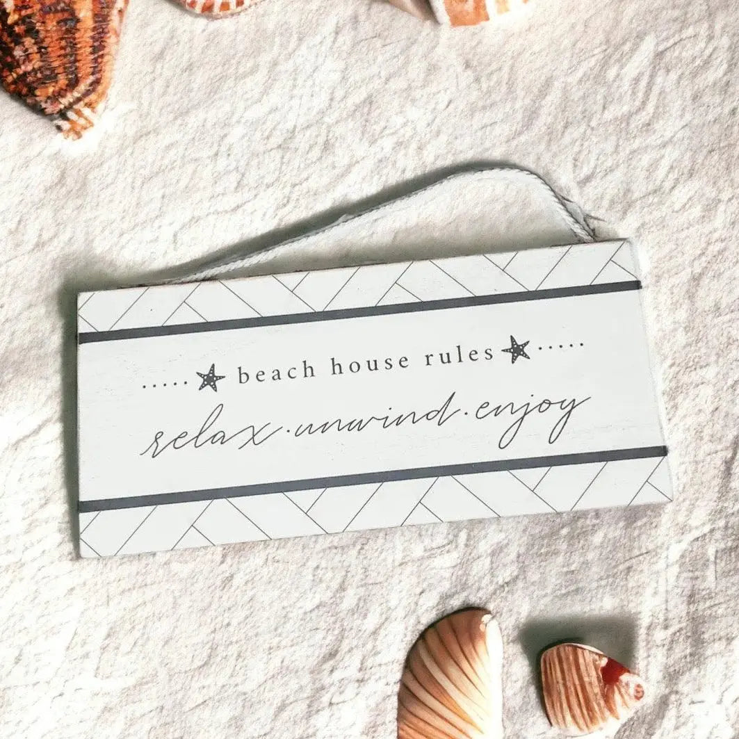 Beach house rules sign with relax unwind enjoy text, surrounded by seashells on a cozy fabric background