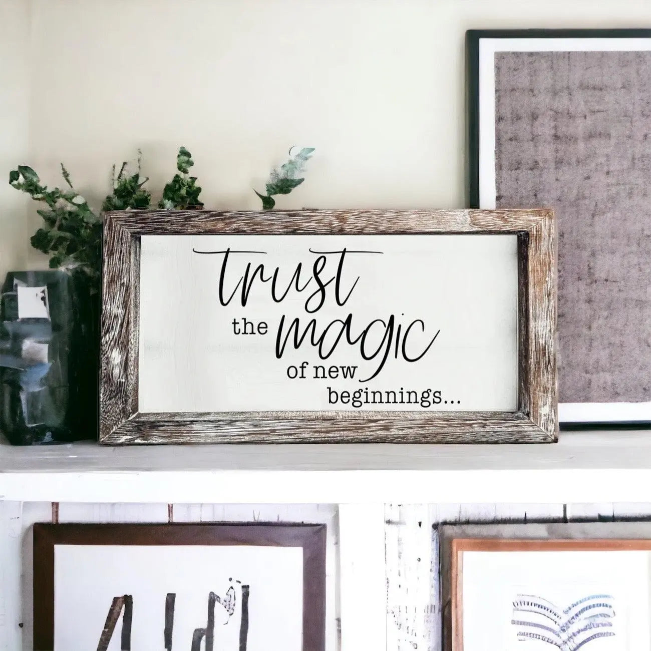 Decorative sign with 'Trust the magic of new beginnings' text in a rustic frame on a shelf.