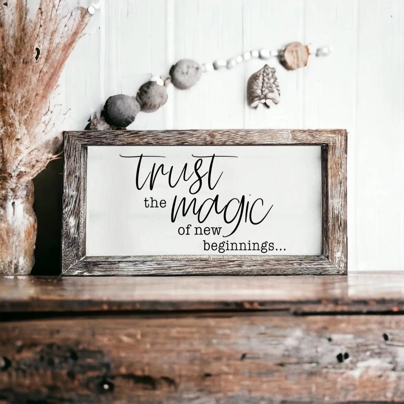 Wooden sign with 'Trust the magic of new beginnings' text on a rustic shelf.
