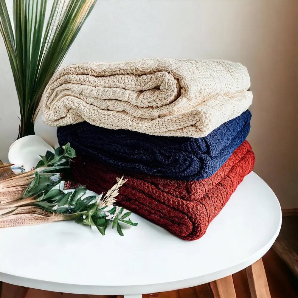 Cozy cable knit blankets in cream, navy, and red, styled on a white table with greenery for farmhouse decor