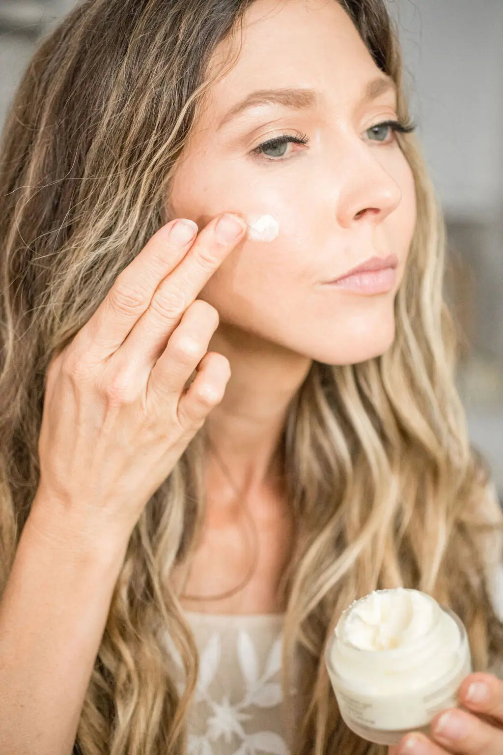 Woman applying creamy face moisturizer from jar, natural skincare routine