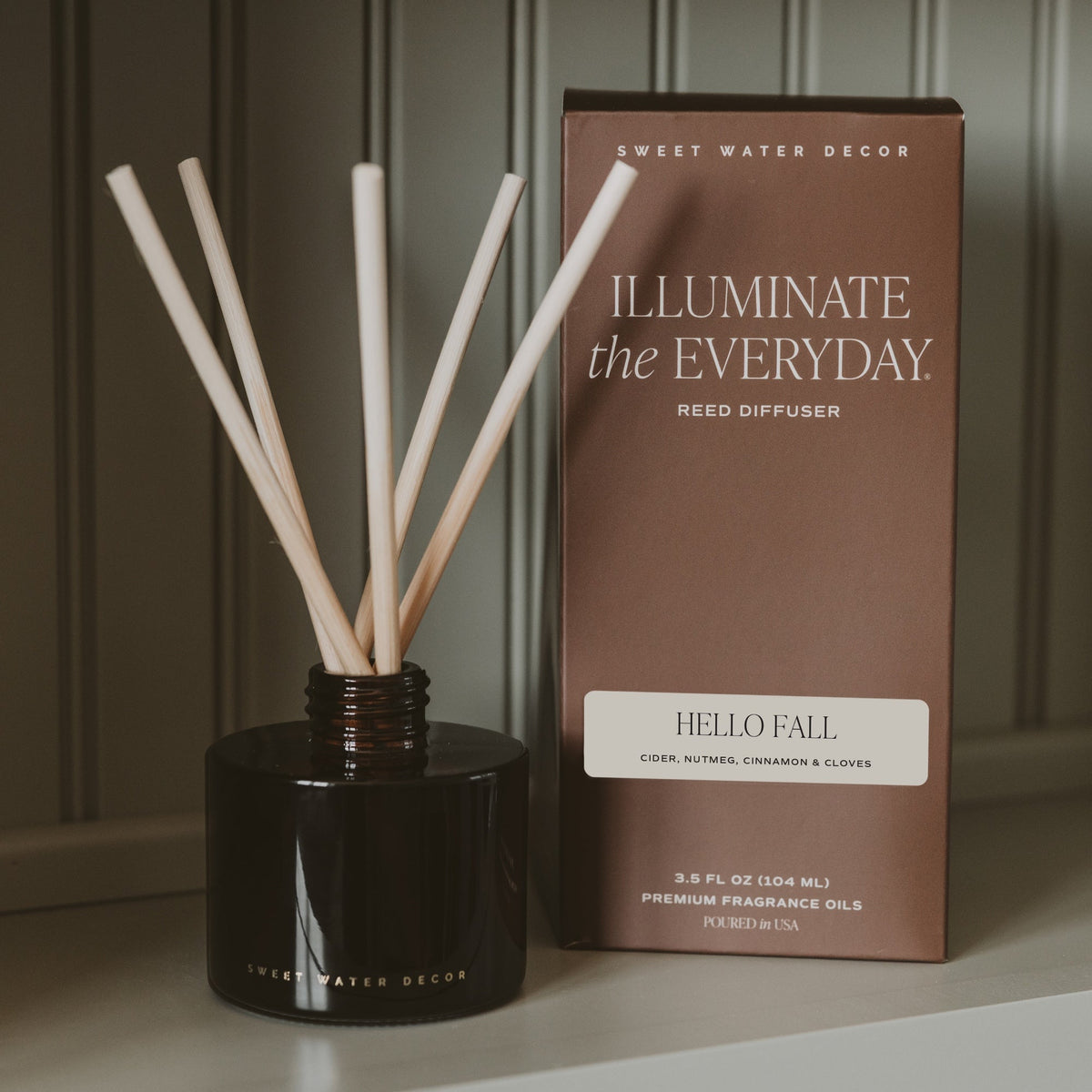 Reed diffuser with wooden sticks and packaging labeled 'Illuminate the Everyday' by Sweet Water Decor on a neutral background.