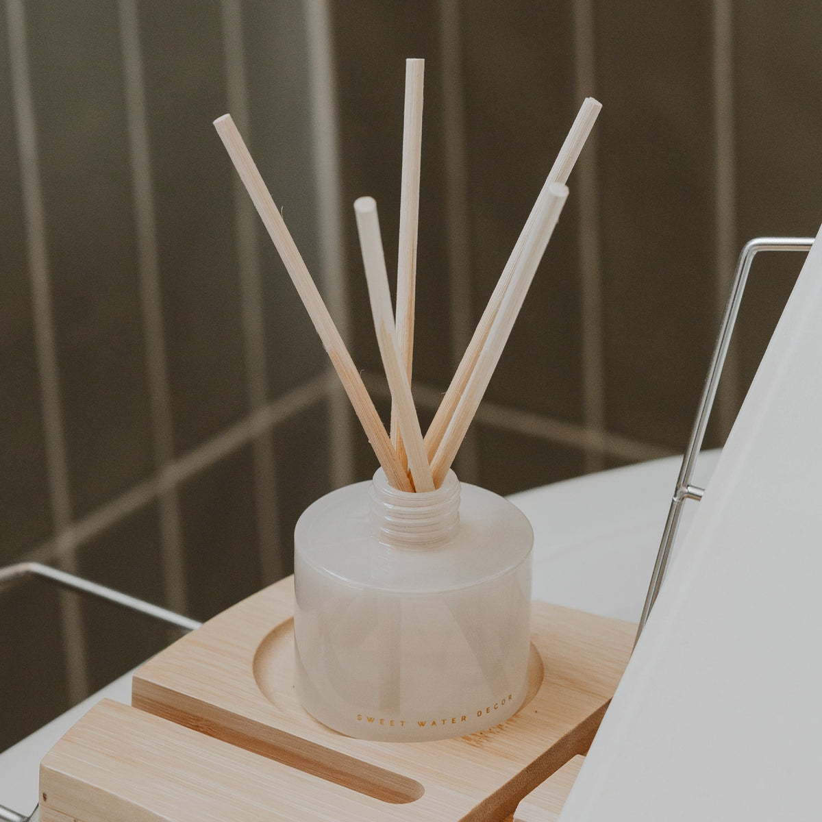 White diffuser with wooden sticks on a wooden stand against a tiled wall background