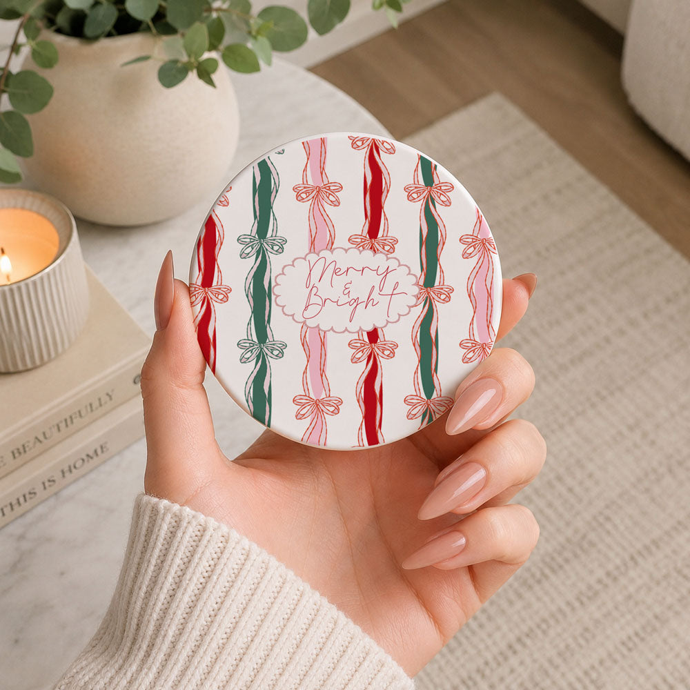 Hand holding a round Christmas-themed coaster with candy cane and bow design.