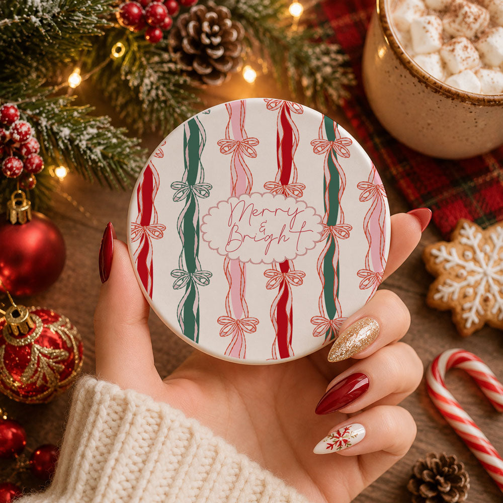 Hand holding a decorative coaster with candy cane design and 'Merry Bright' text, surrounded by Christmas decorations.