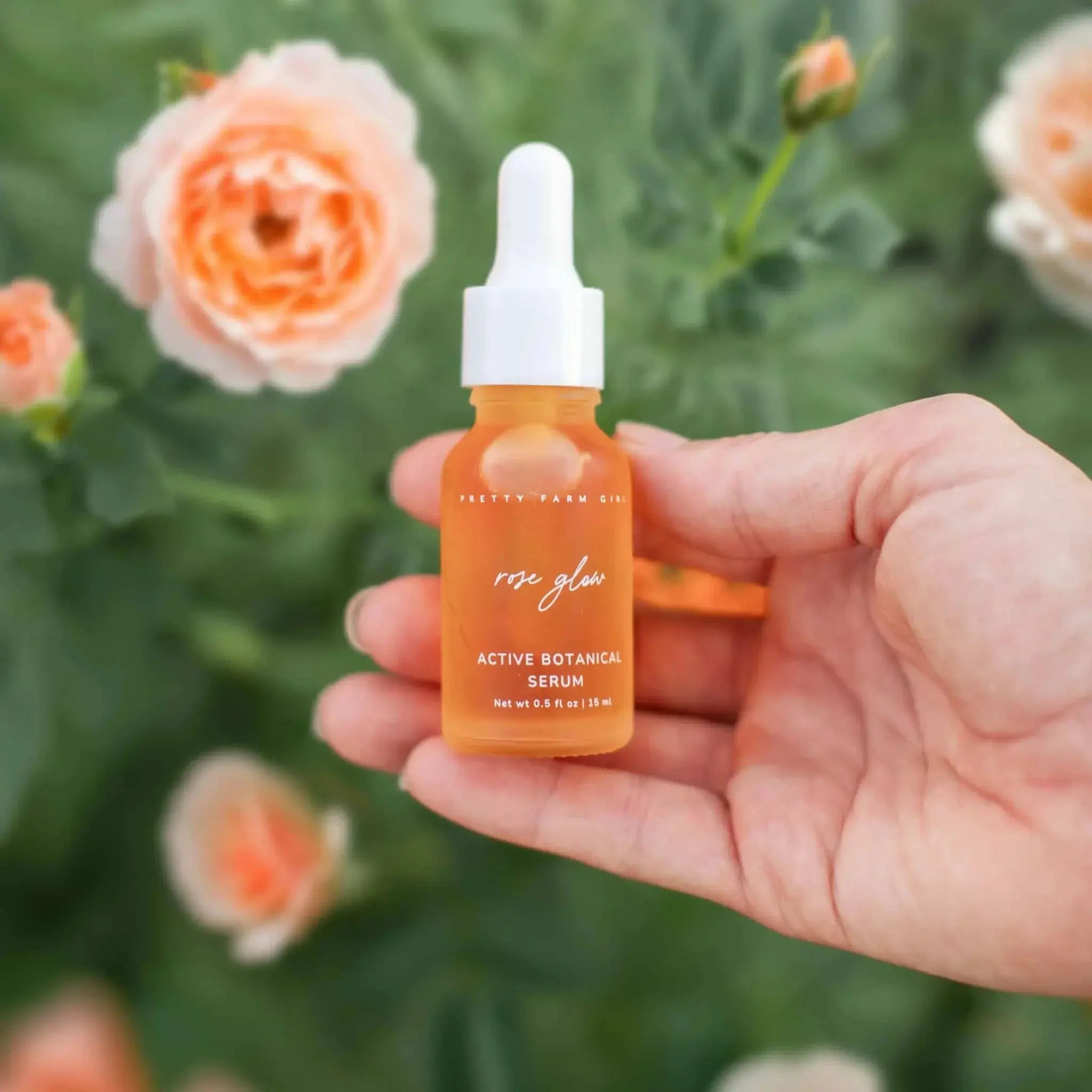 Rose Glow Active Botanical Serum in hand with peach roses, natural skincare for cozy home wellness