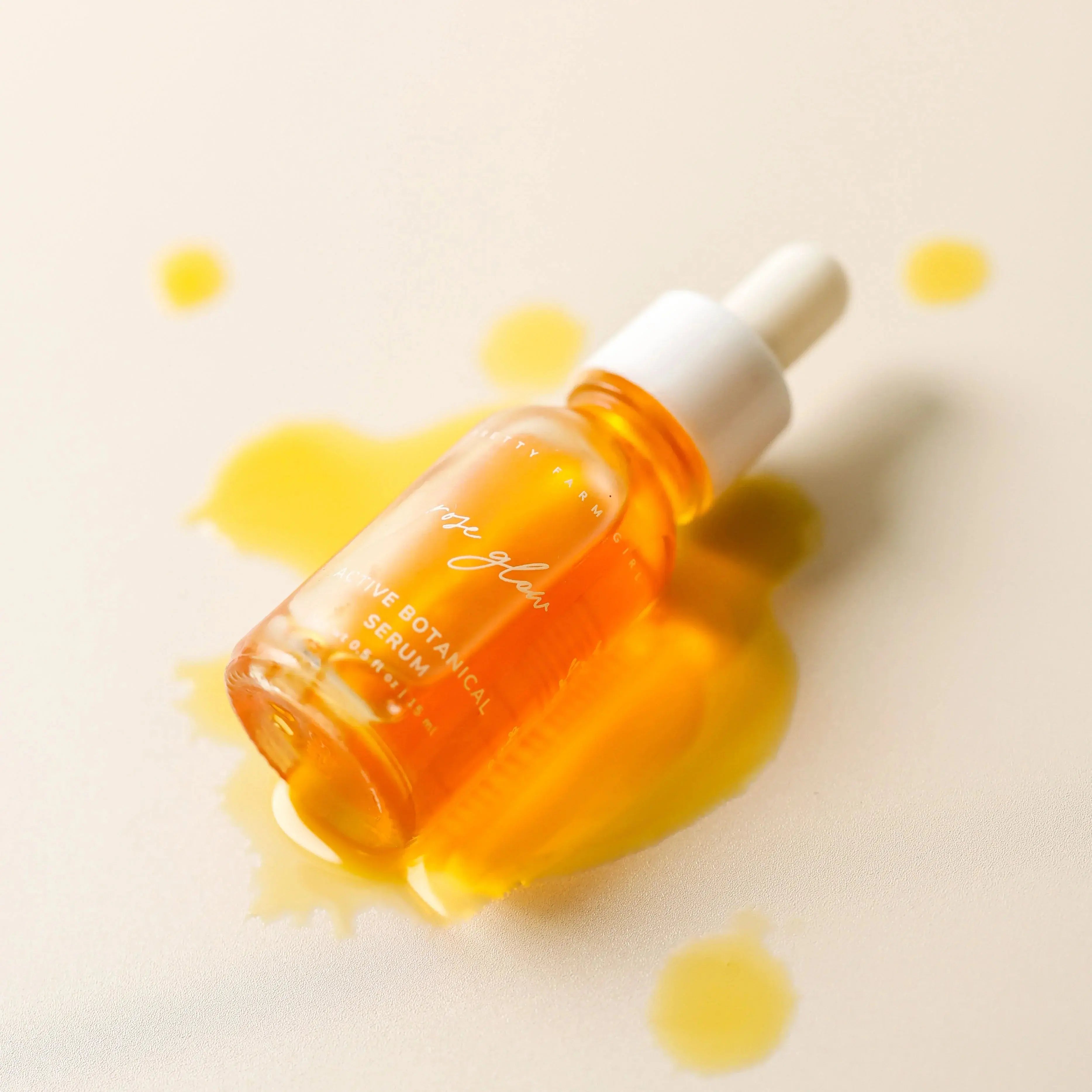Rose Glow Active Botanical Serum in glass dropper bottle with golden oil spill on soft beige background