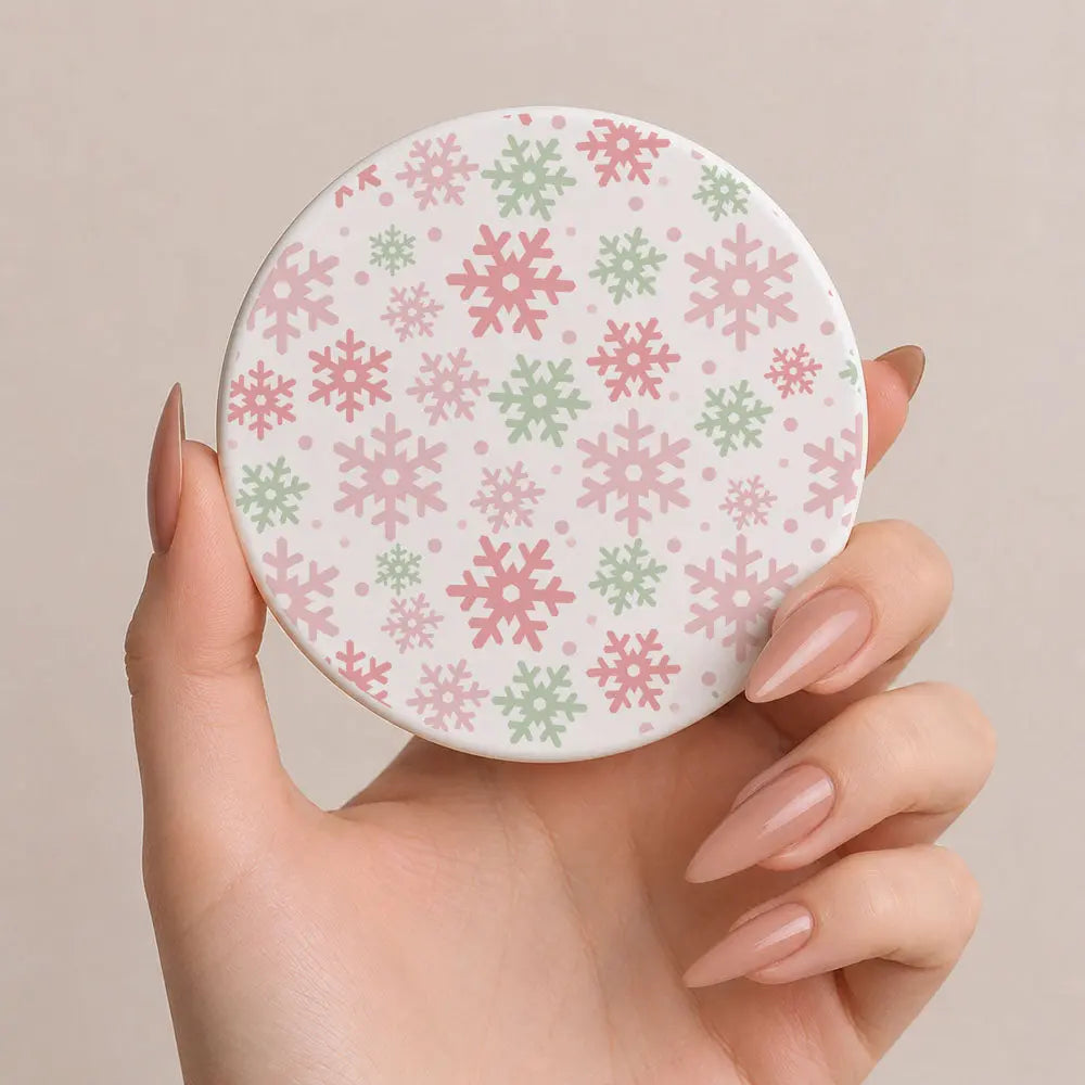 Hand holding a round compact mirror with floral pattern on a beige background