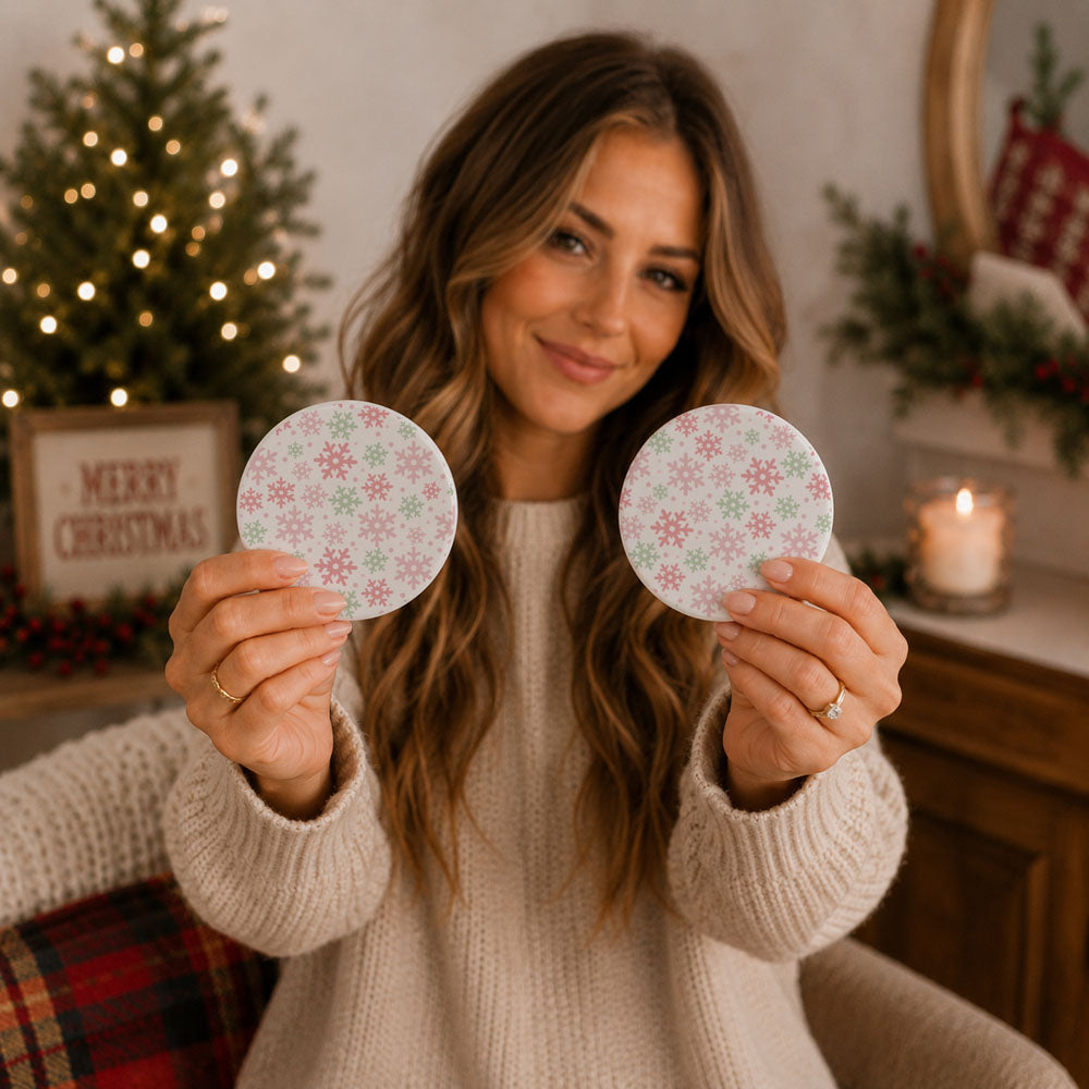 Woman holding two decorative coasters in a cozy room with Christmas decorations.