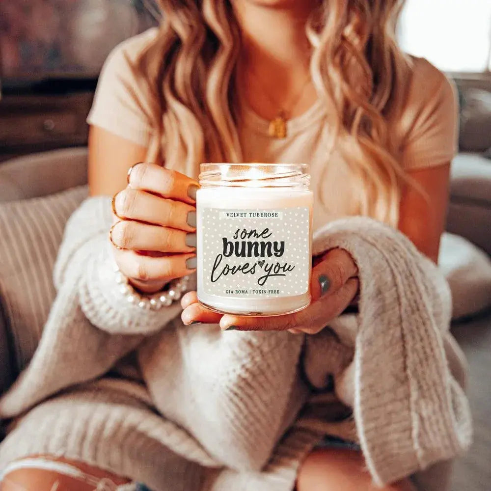 Person holding a candle jar labeled 'some bunny loves you' in a cozy indoor setting.