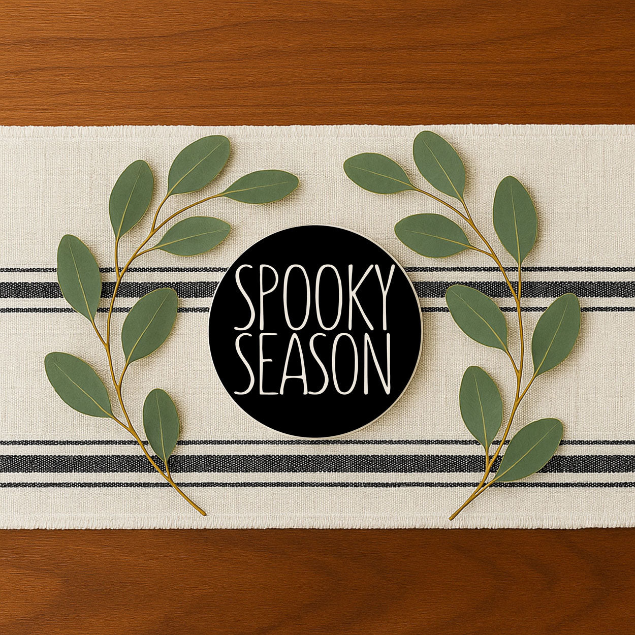 Decorative mat with 'Spooky Season' text and green leaves on a wooden surface