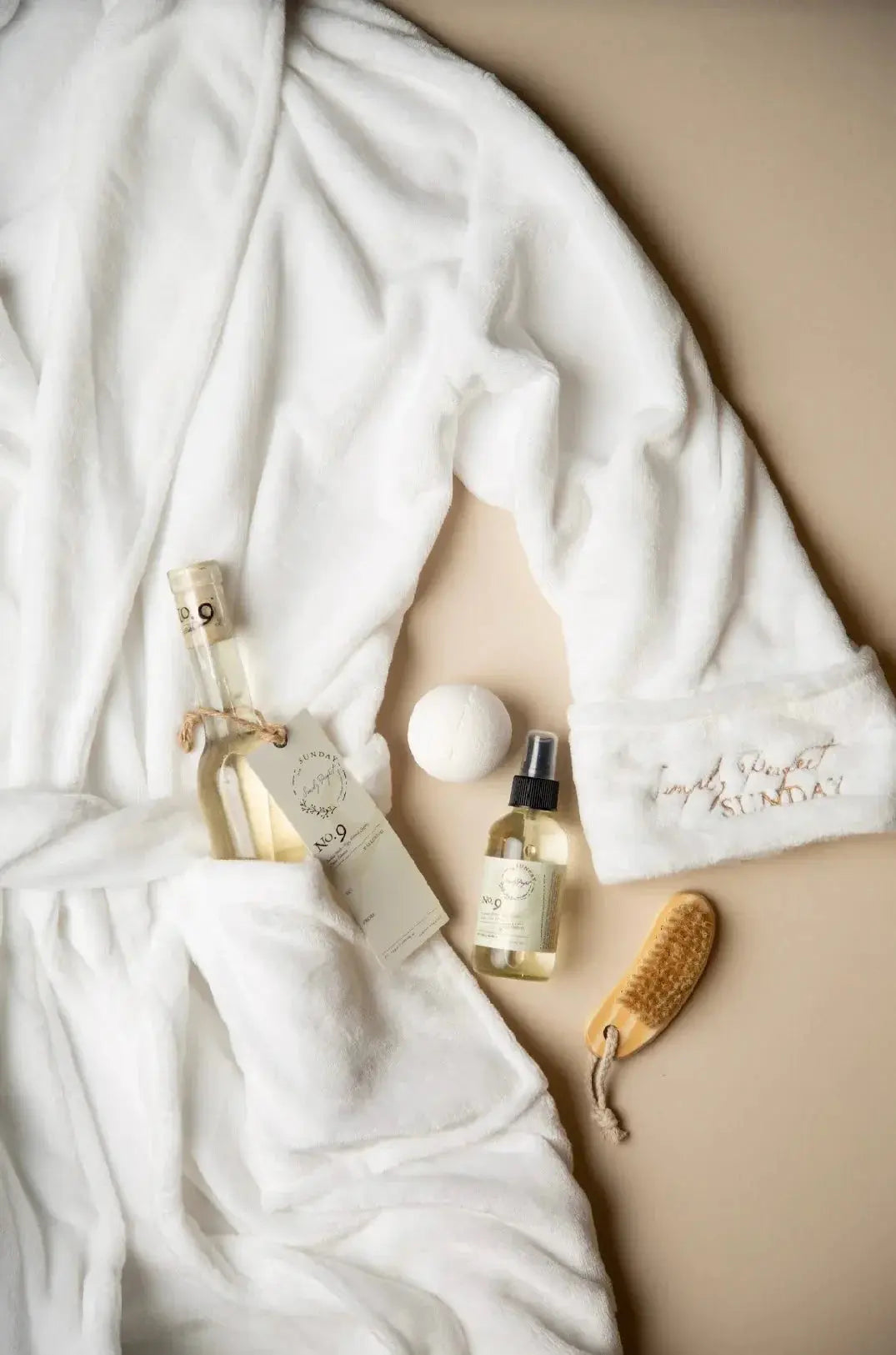 Cozy white robe with 'Simply Perfect Sunday' embroidery, bath products, and body brush for farmhouse spa relaxation