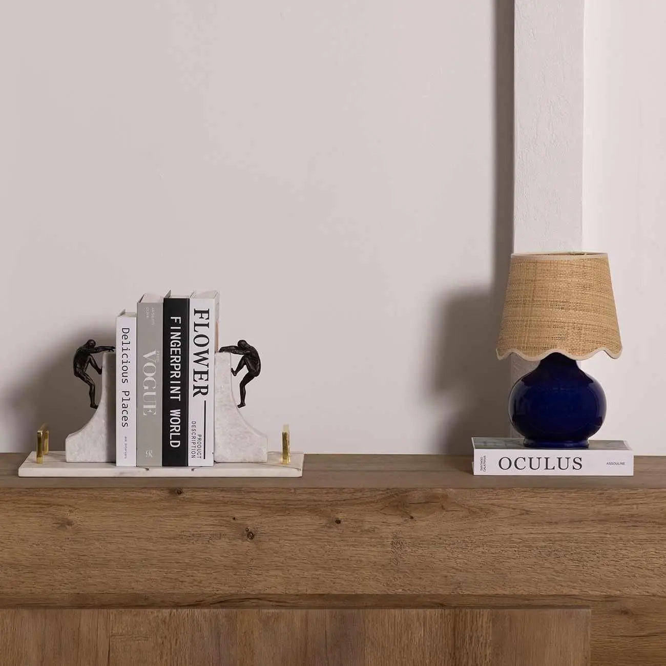 Marble bookends with climbing figures, blue ceramic lamp, and books on rustic wood shelf for cozy home decor
