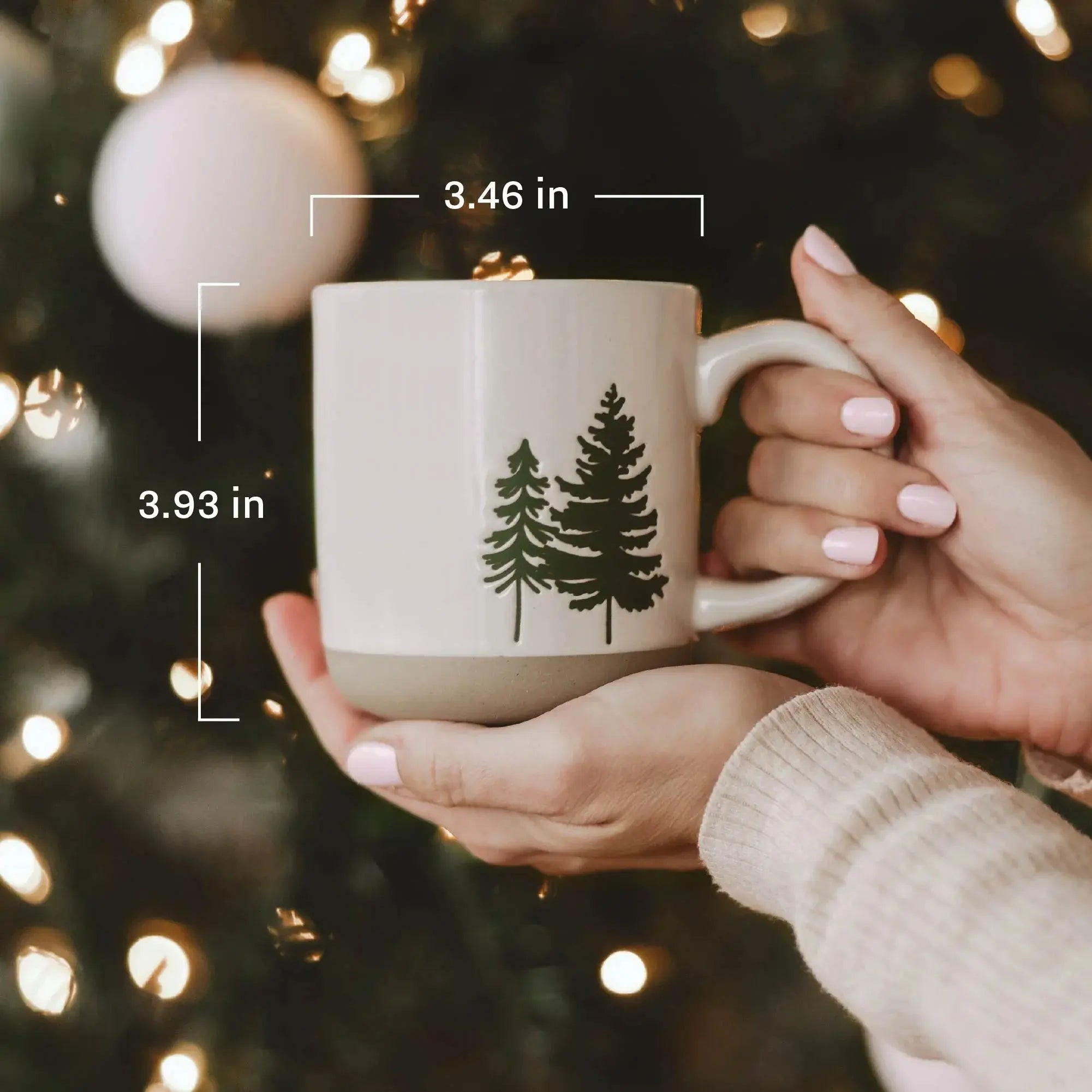Cozy ceramic mug with pine tree design, held near Christmas tree lights, perfect for farmhouse or cottage decor