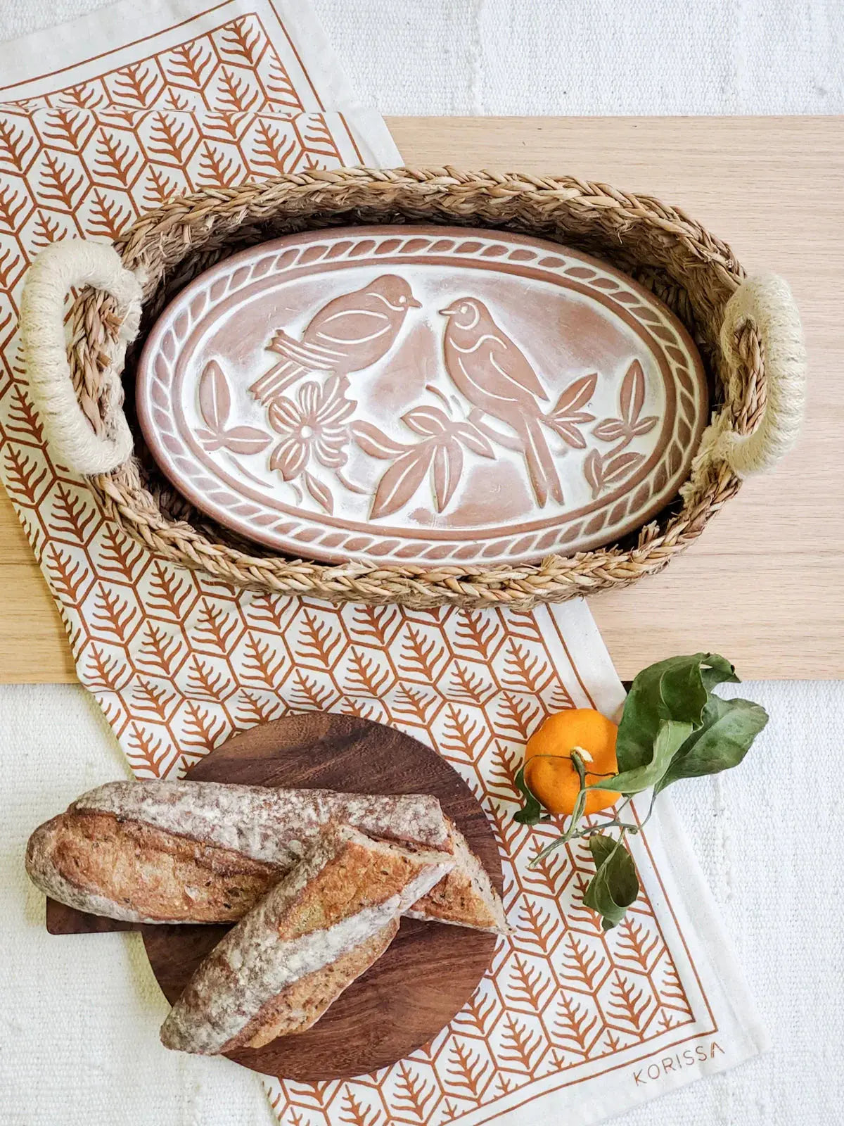 Farmhouse ceramic bird platter in woven tray with bread, orange, and leaf-patterned napkin for cozy kitchen decor