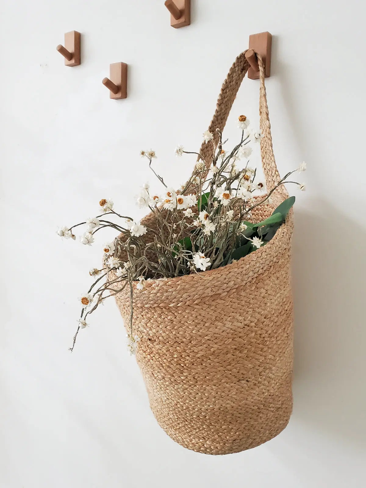 Woven seagrass basket with dried white daisies hanging on wooden wall hooks, farmhouse decor