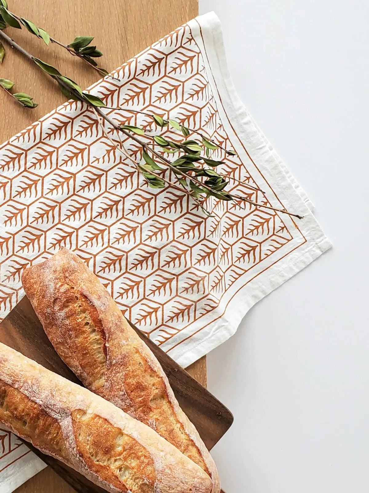 Farmhouse-style tea towel with leaf pattern, paired with fresh bread on wooden board