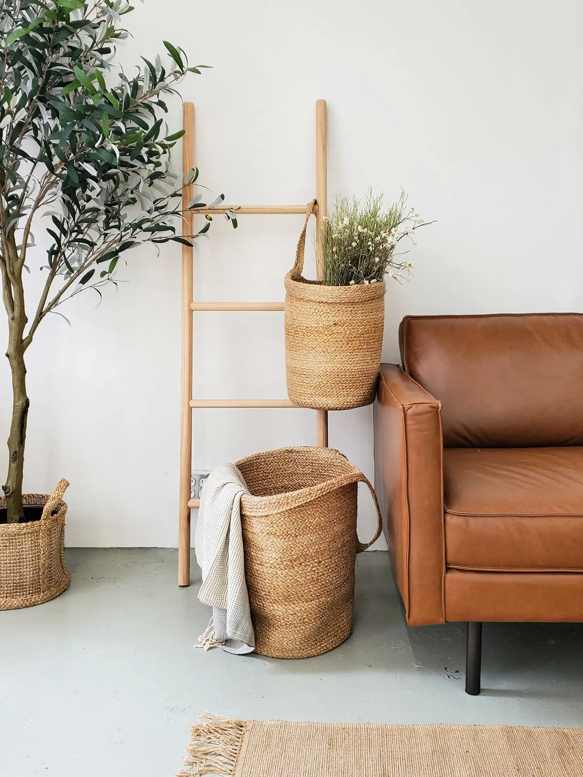Cozy farmhouse living room with woven baskets, wooden ladder, leather armchair, and olive tree