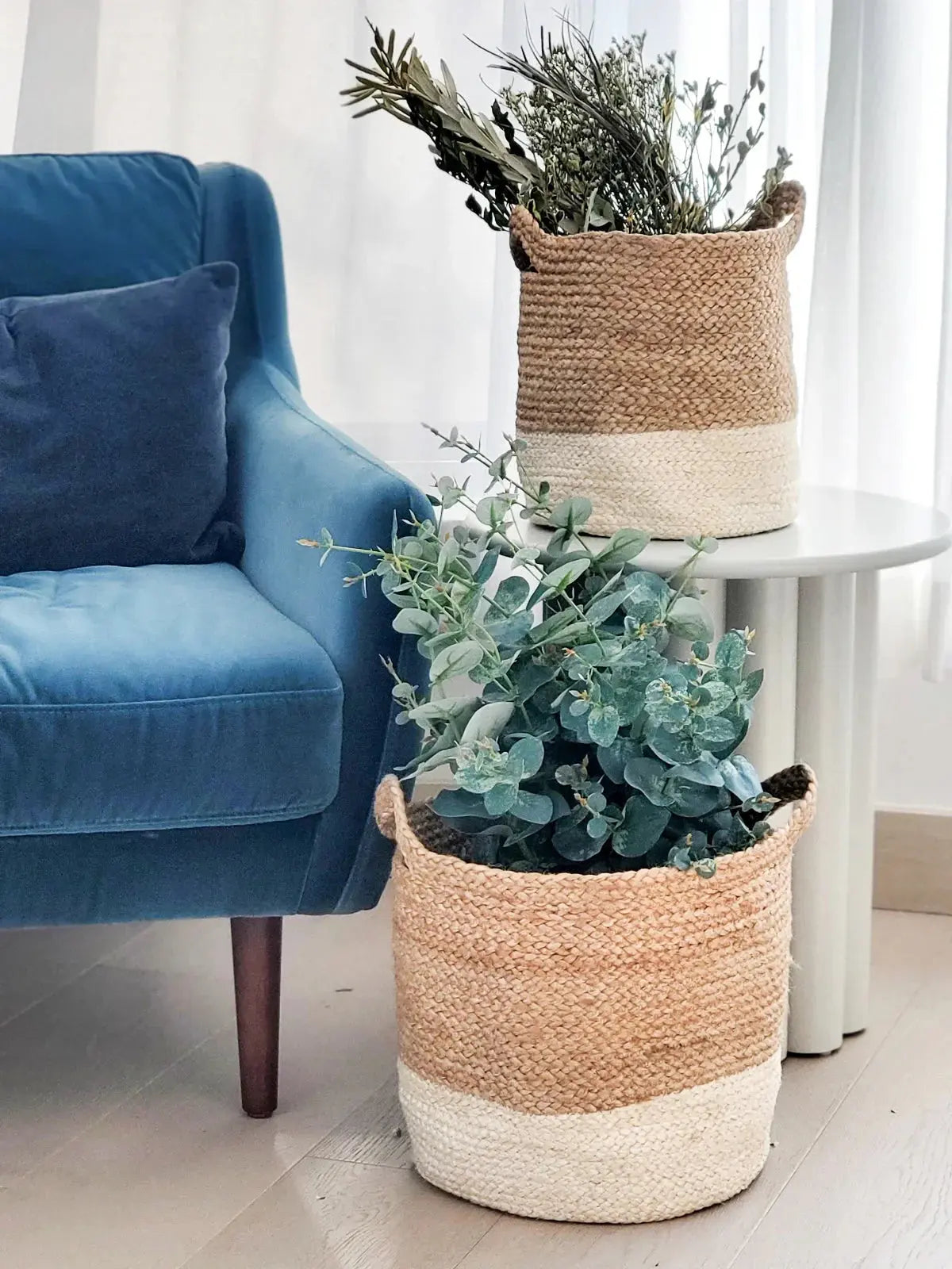 Cozy farmhouse decor with woven baskets holding dried greenery beside a blue velvet armchair