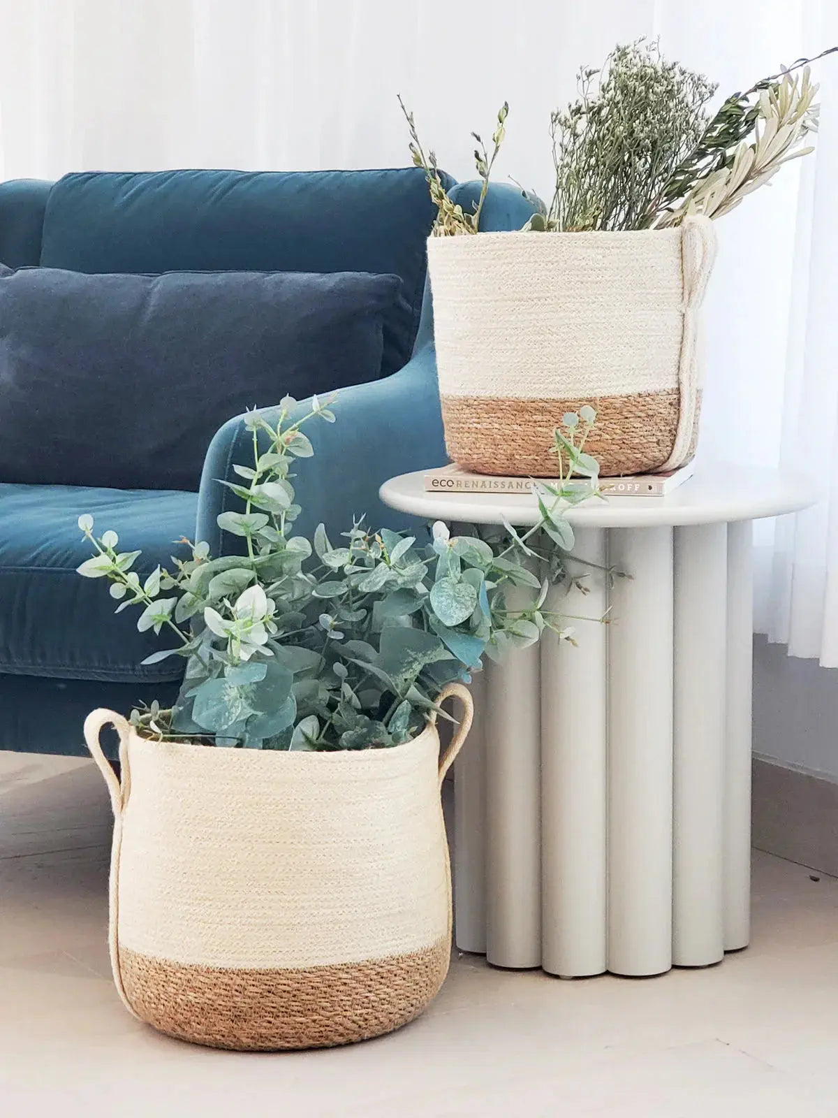 Cozy farmhouse decor with woven baskets holding eucalyptus and dried flowers beside a teal velvet sofa
