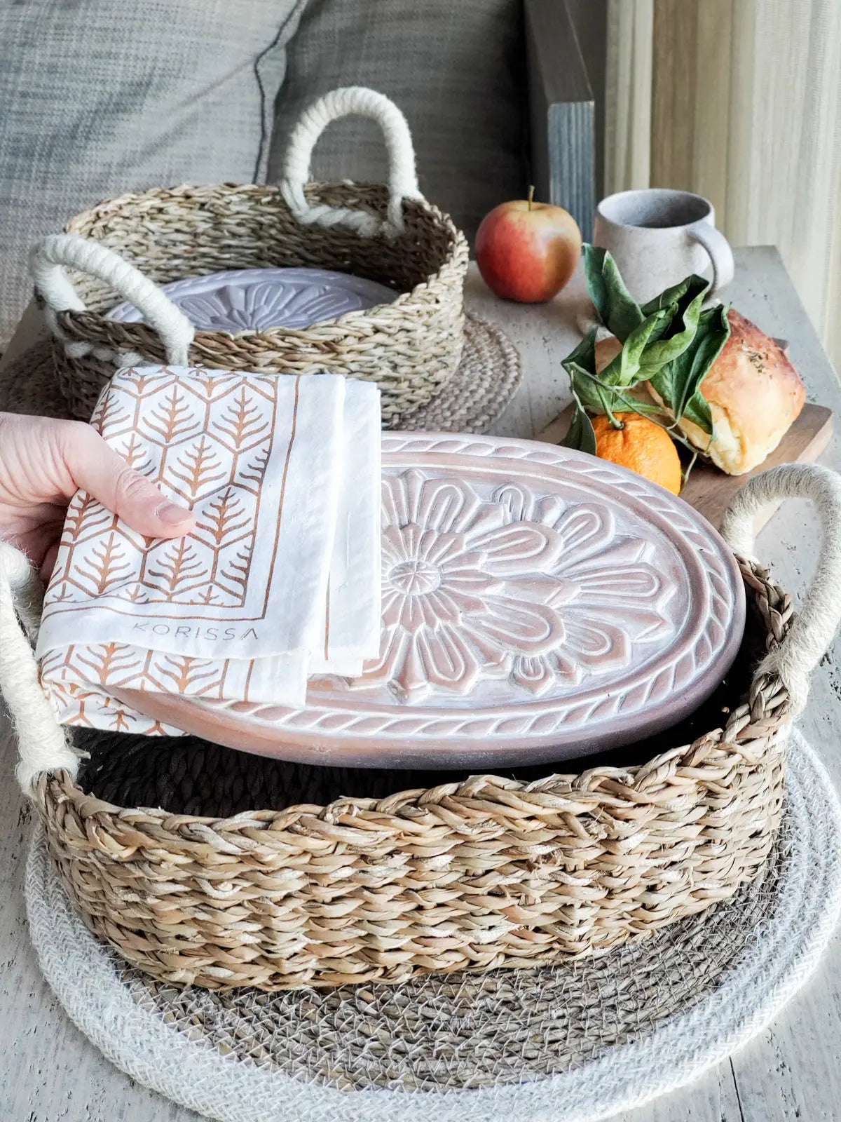 Cozy farmhouse decor with woven basket, embossed tray, leaf-pattern napkin, and fresh fruit for rustic home styling