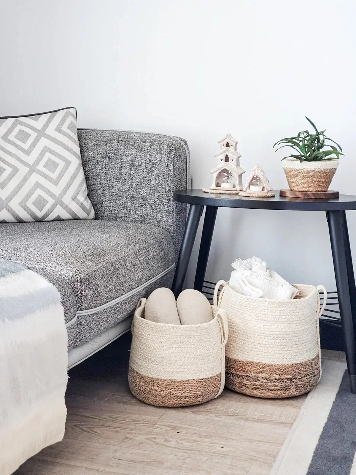 Cozy farmhouse living room with gray sofa, woven baskets, and decorative side table with plants and candle holders