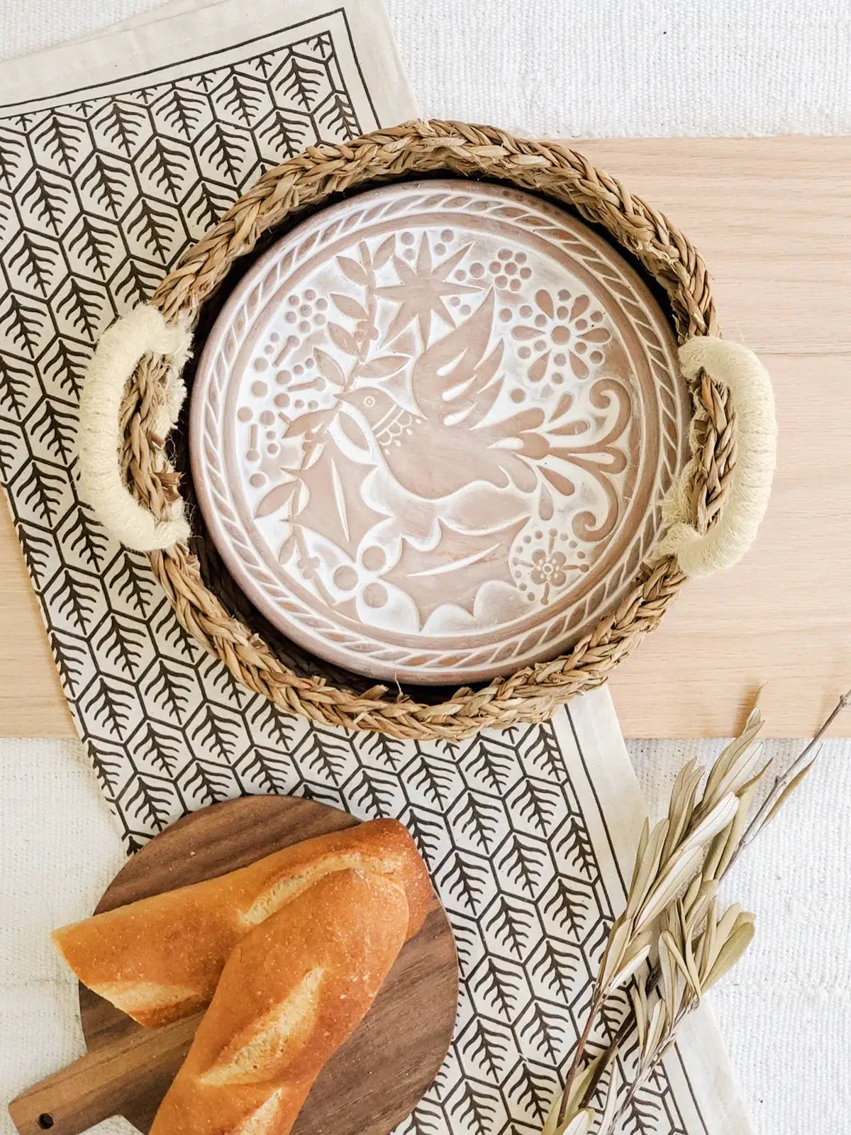 Woven tray with carved ceramic plate, bread, and leaf-patterned napkin for cozy farmhouse decor