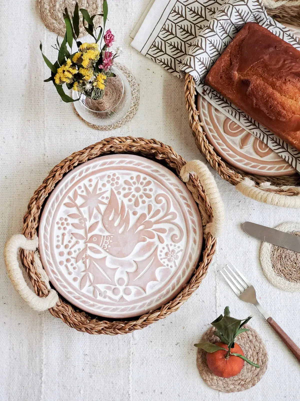 Handcrafted ceramic plate with bird motif in woven tray, farmhouse table setting with bread and wildflowers