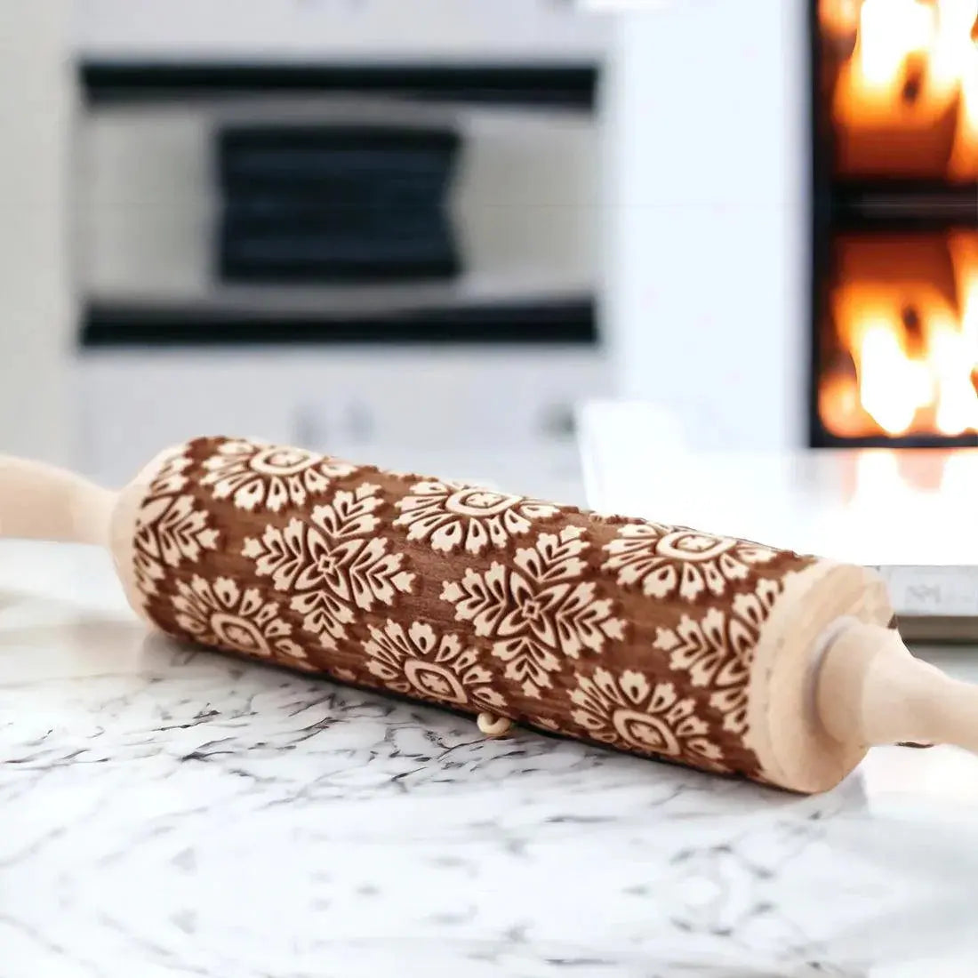 Decorative rolling pin with snowflake patterns on a marble surface with a blurred background of a fireplace.