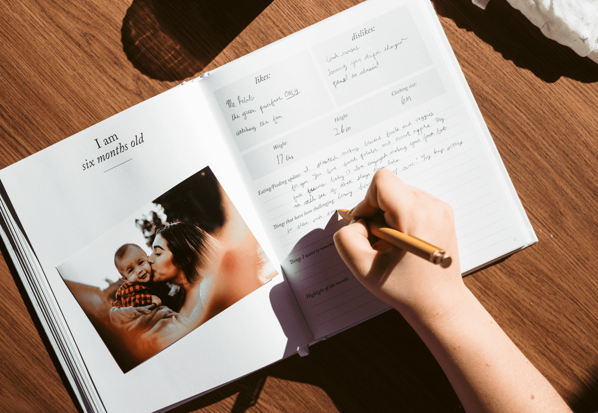 Open book with a photo of a baby and text, being written on with a pen.