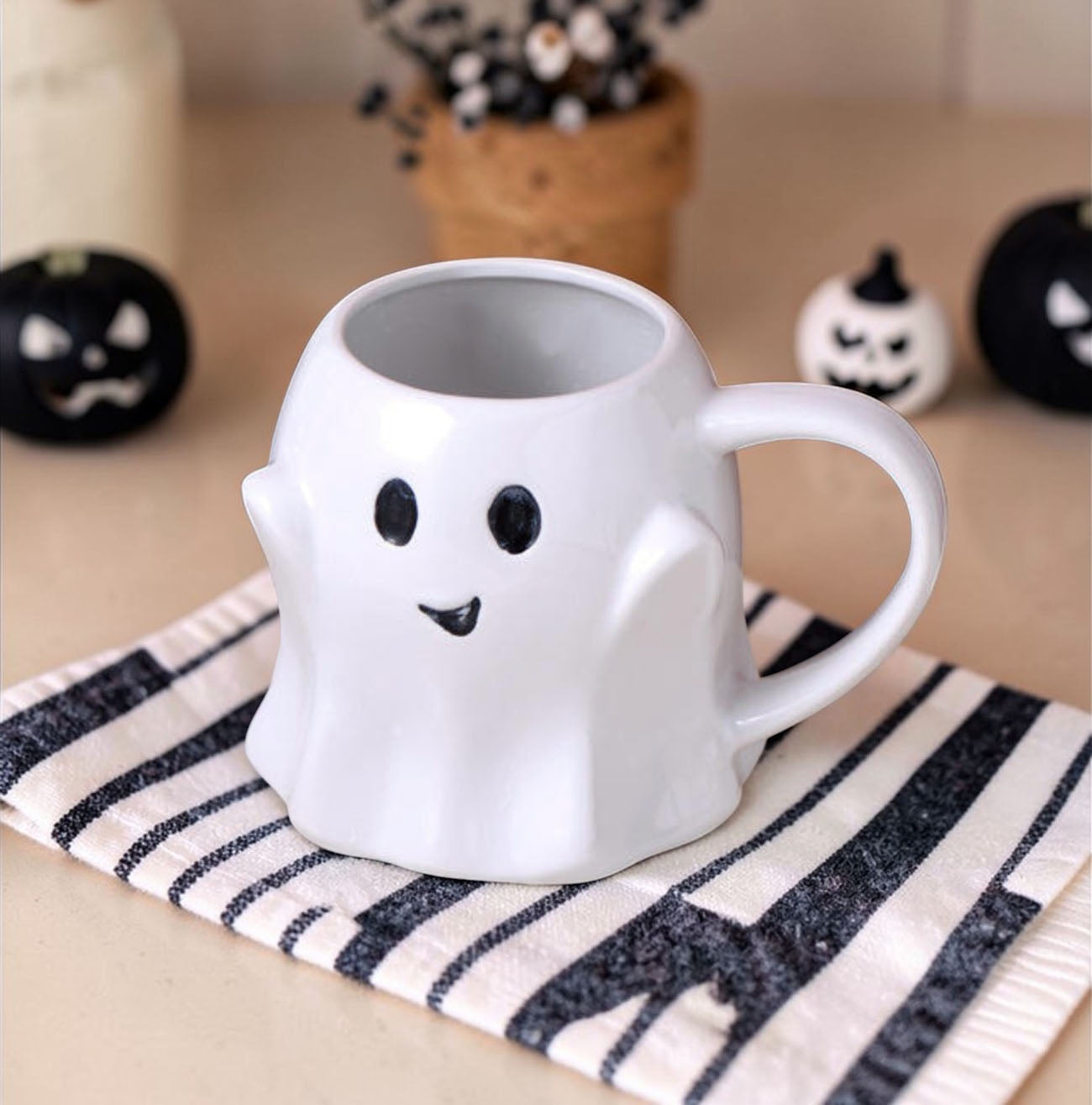 Ghost-shaped mug on a striped cloth with Halloween decorations in the background
